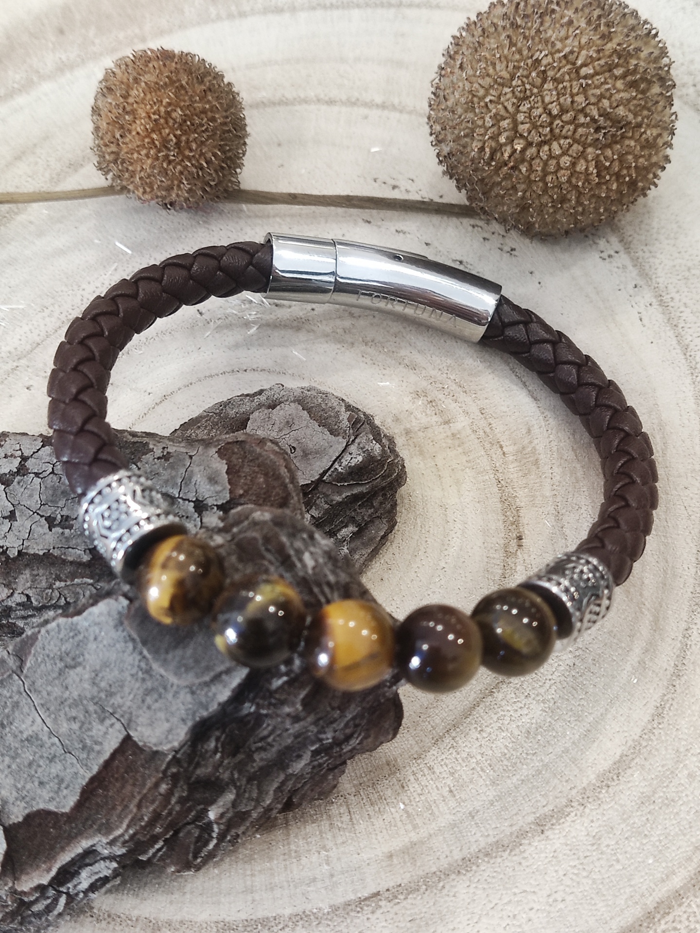 Pulseira de pele castanha com contas castanhas e amarelas e fecho metálico sobre superfície de madeira clara