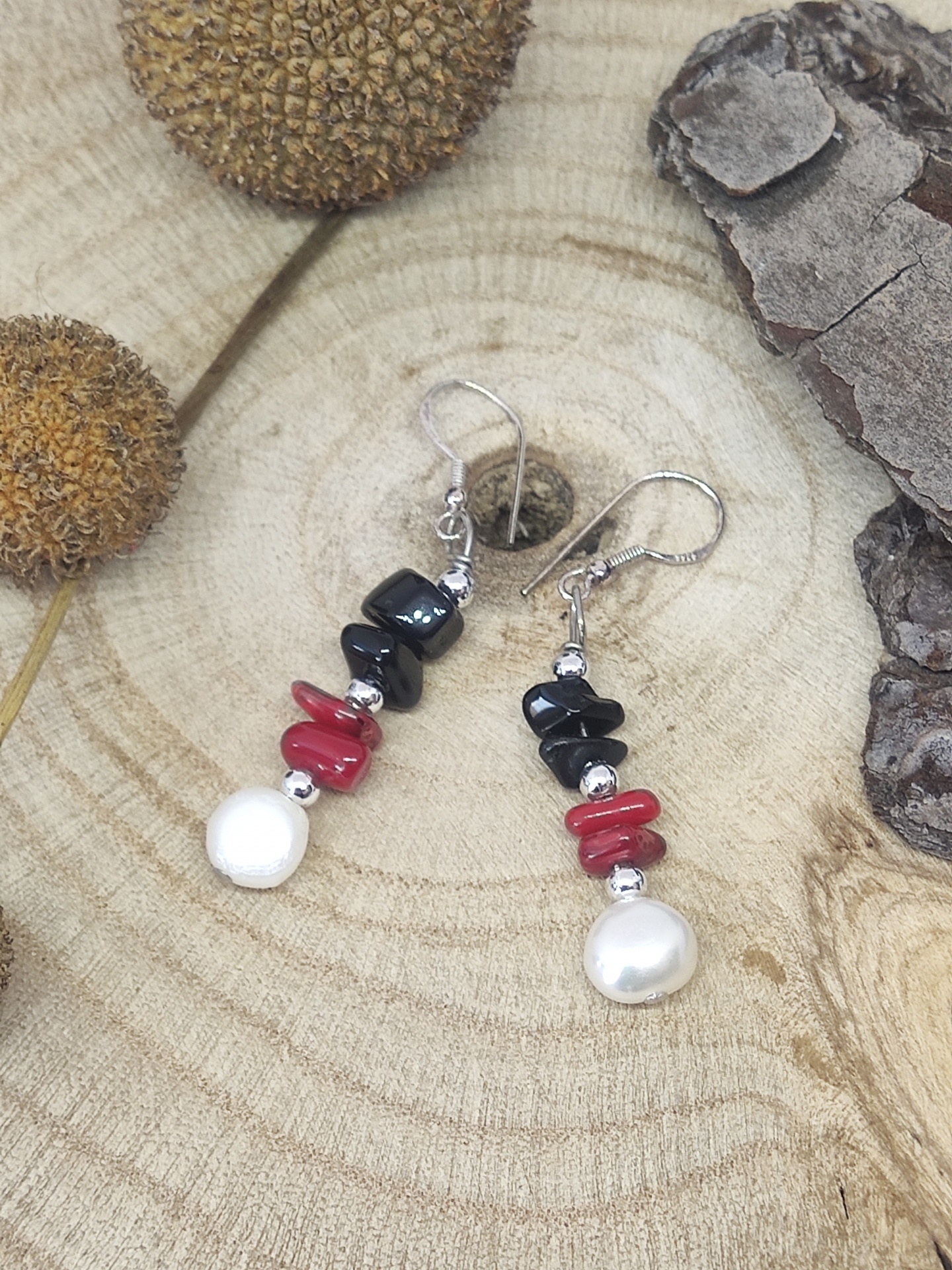 Brincos pendentes com pedras pretas, vermelhas, pérolas brancas e metais prateados sobre madeira clara