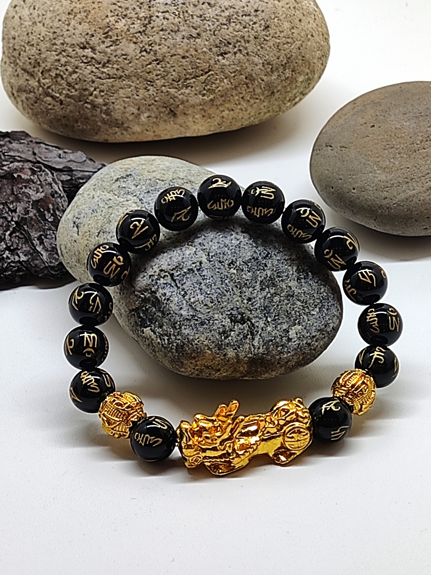 Pulseira preta com inscrições douradas e peça central dourada em forma de dragão sobre pedras lisas