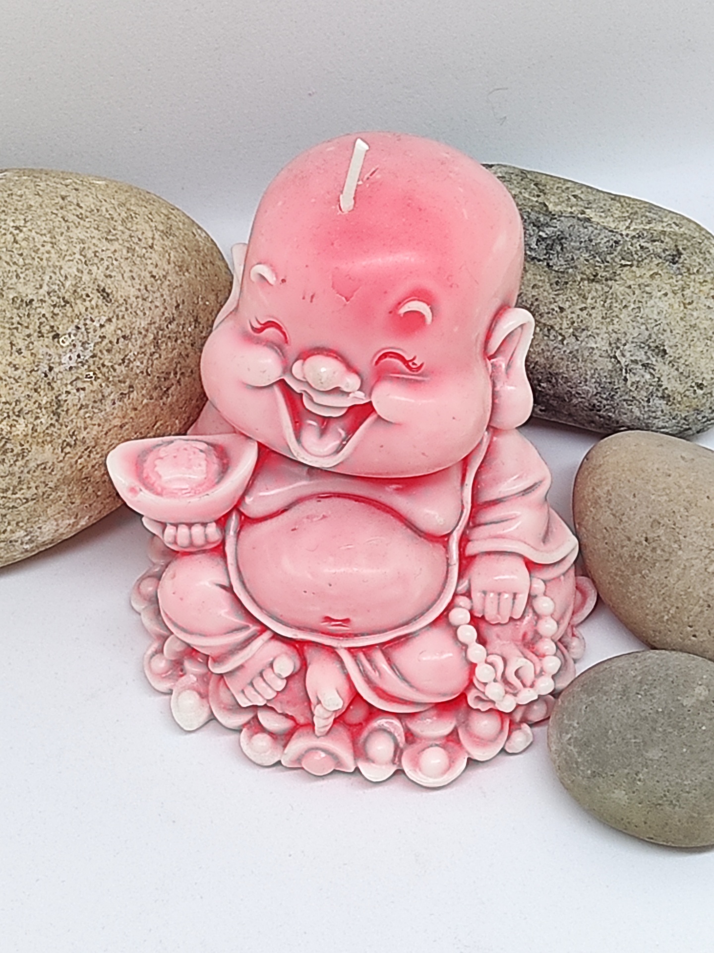 Vela rosa em forma de Buda sorridente com quatro pedras ao redor