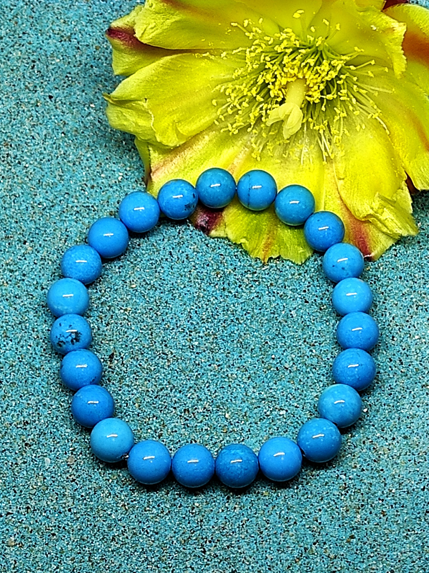 Pulseira azul em contas esféricas com flor amarela e areia azul