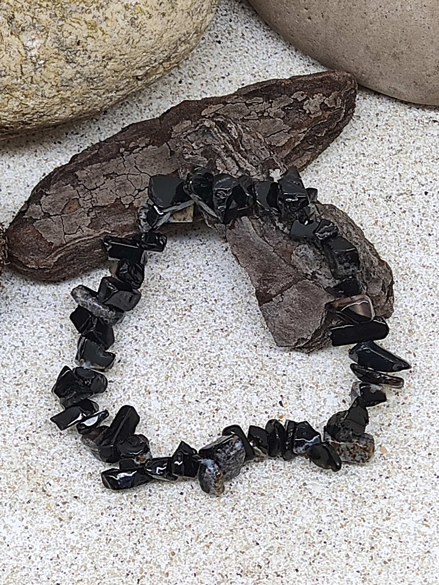 Pulseira de pedras pretas brilhantes sobre superfície clara com pedras ao redor