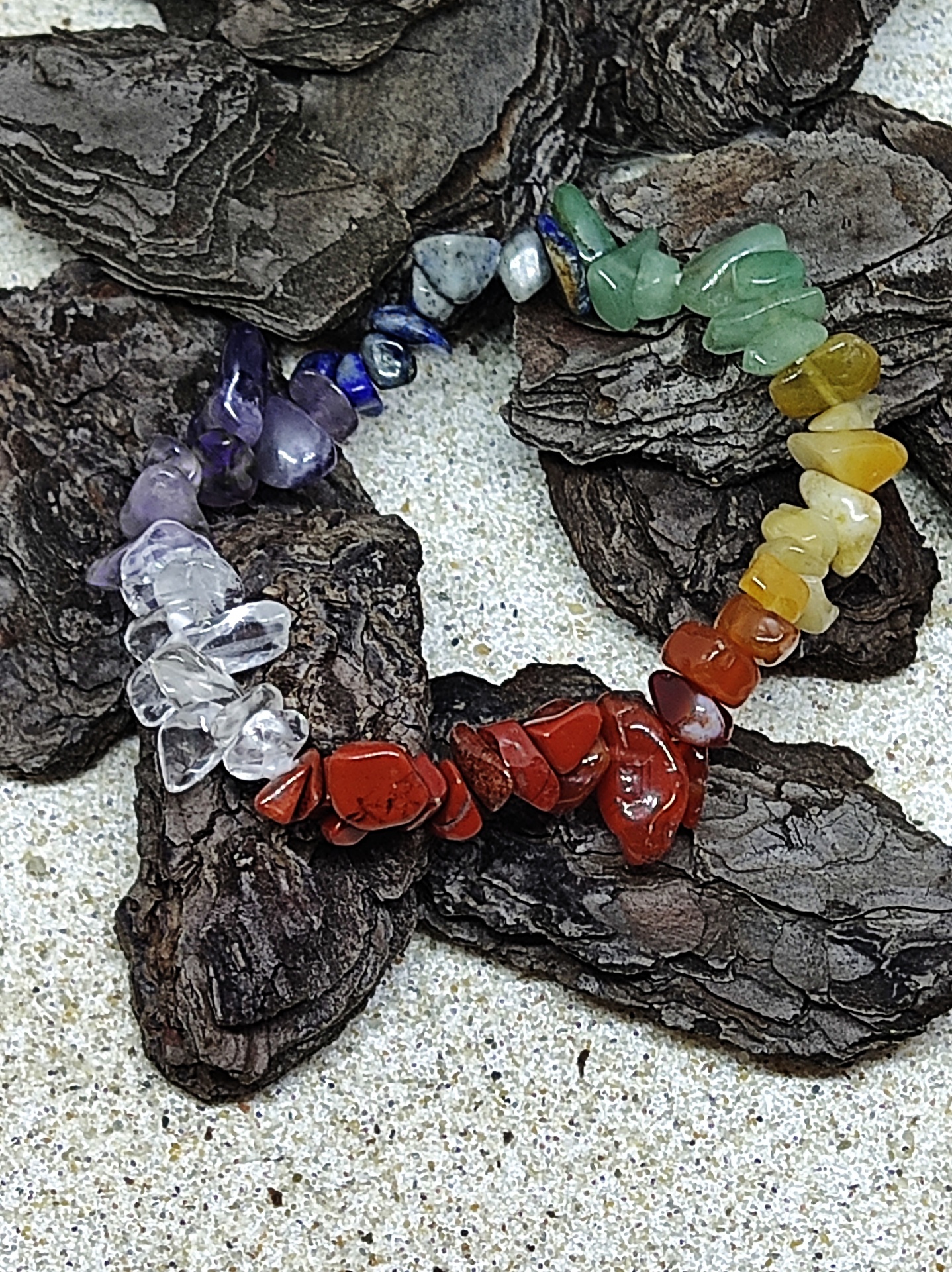 Pulseira colorida de pedras naturais sobre casca de árvore e fundo arenoso