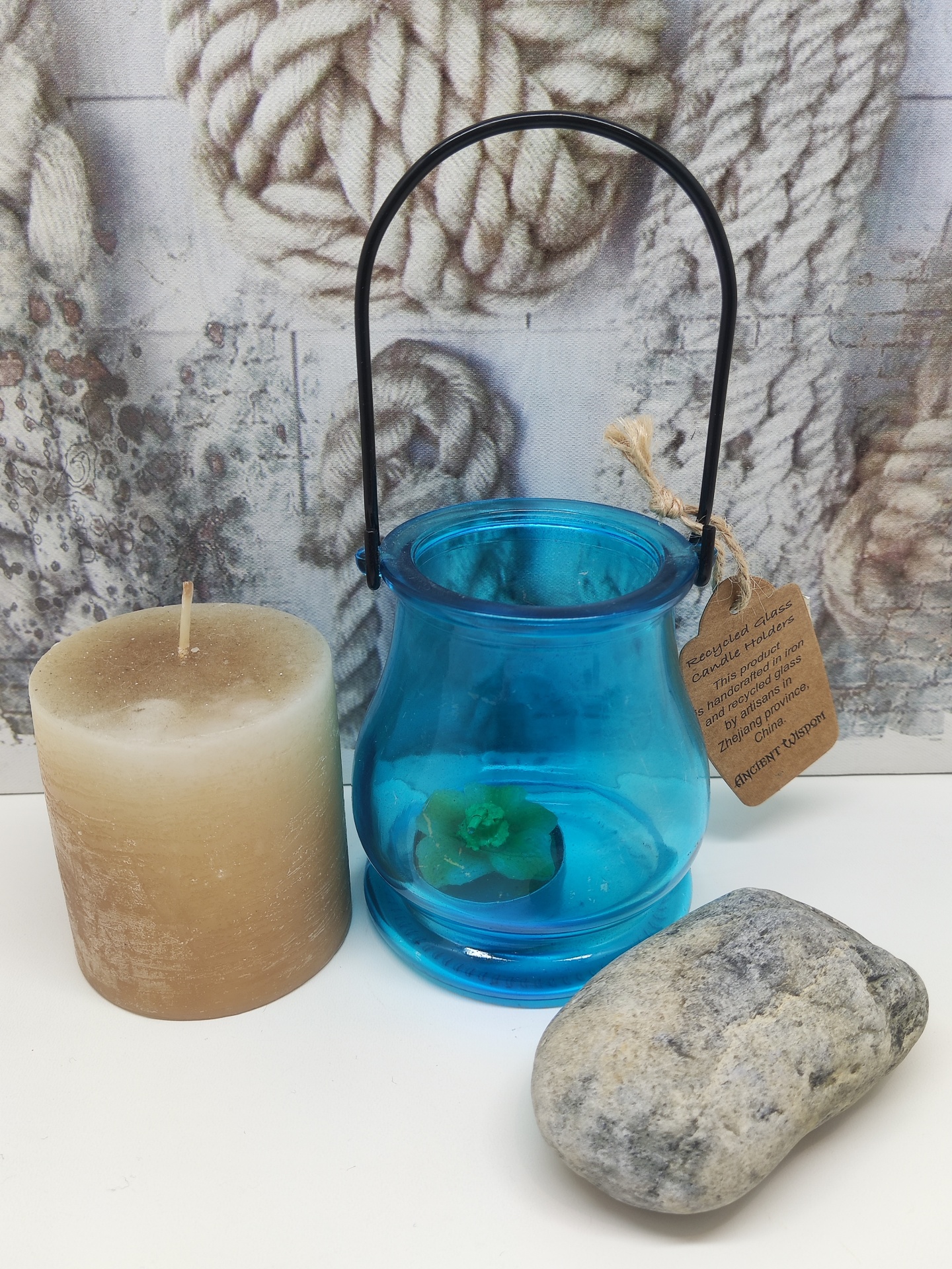 Vela castanha, vaso azul de vidro com planta verde e pedra cinzenta sobre superfície branca