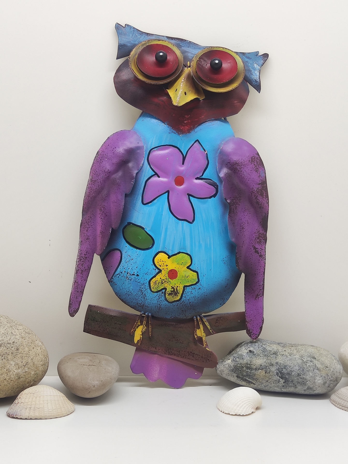 Estátua decorativa de coruja colorida com flores sobre branca e pedras