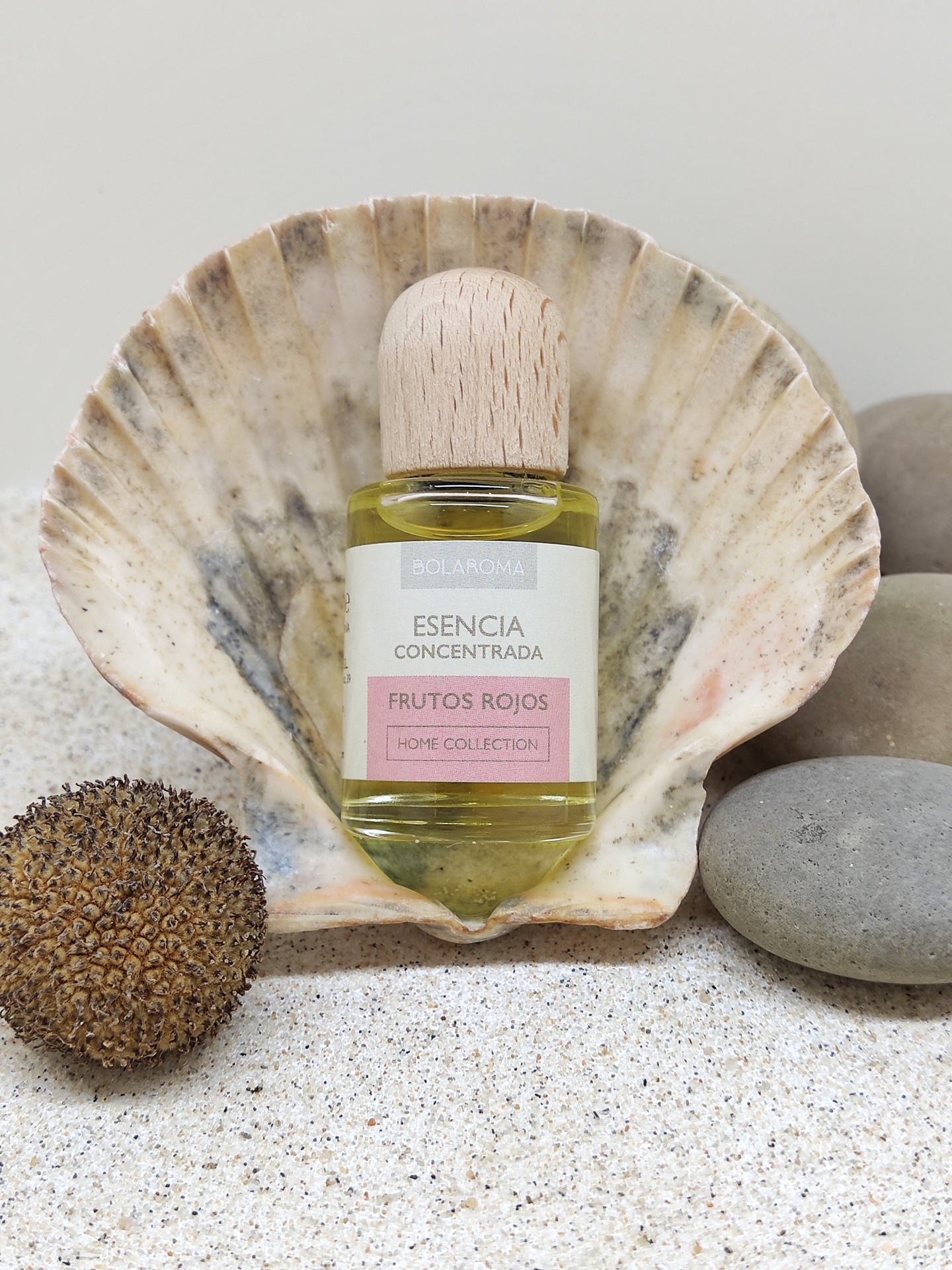 Frasco de essência concentrada Frutos Rojos em concha marinha com pedras e areia