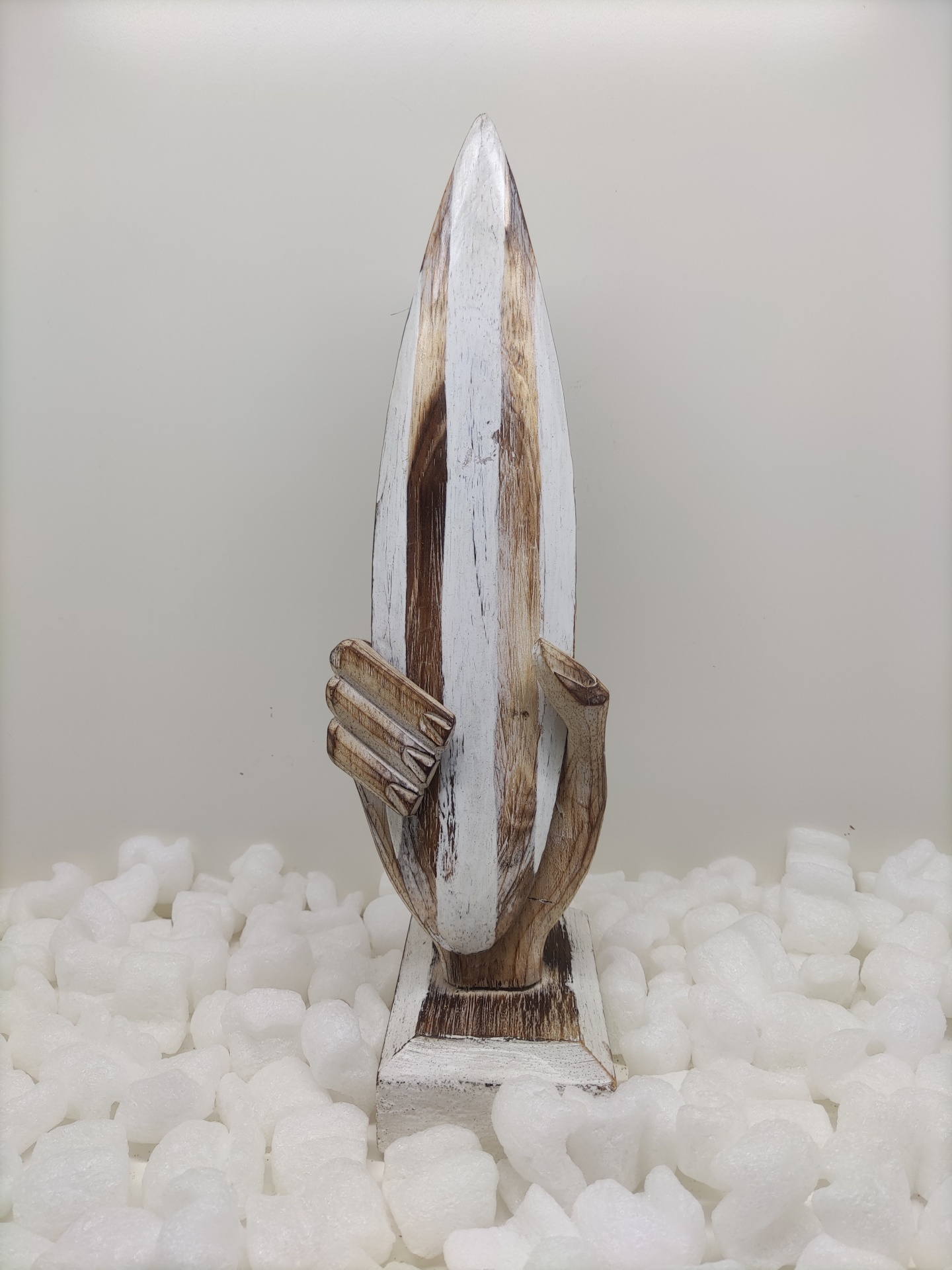 Escultura de madeira de uma mão segurando uma prancha de surf em branco e castanho