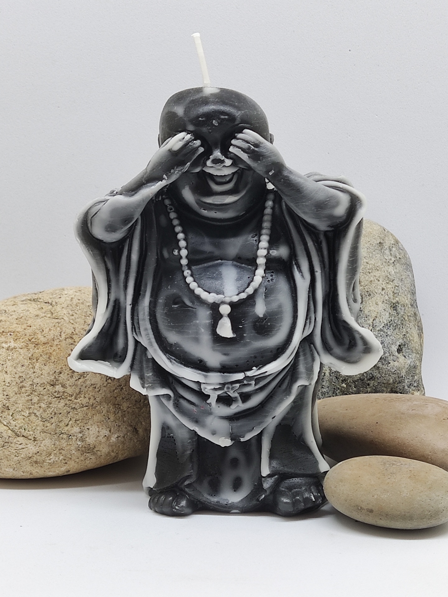 Vela decorativa de Buda tapando os olhos com padrão marmoreado preto e branco e pedras naturais ao redor