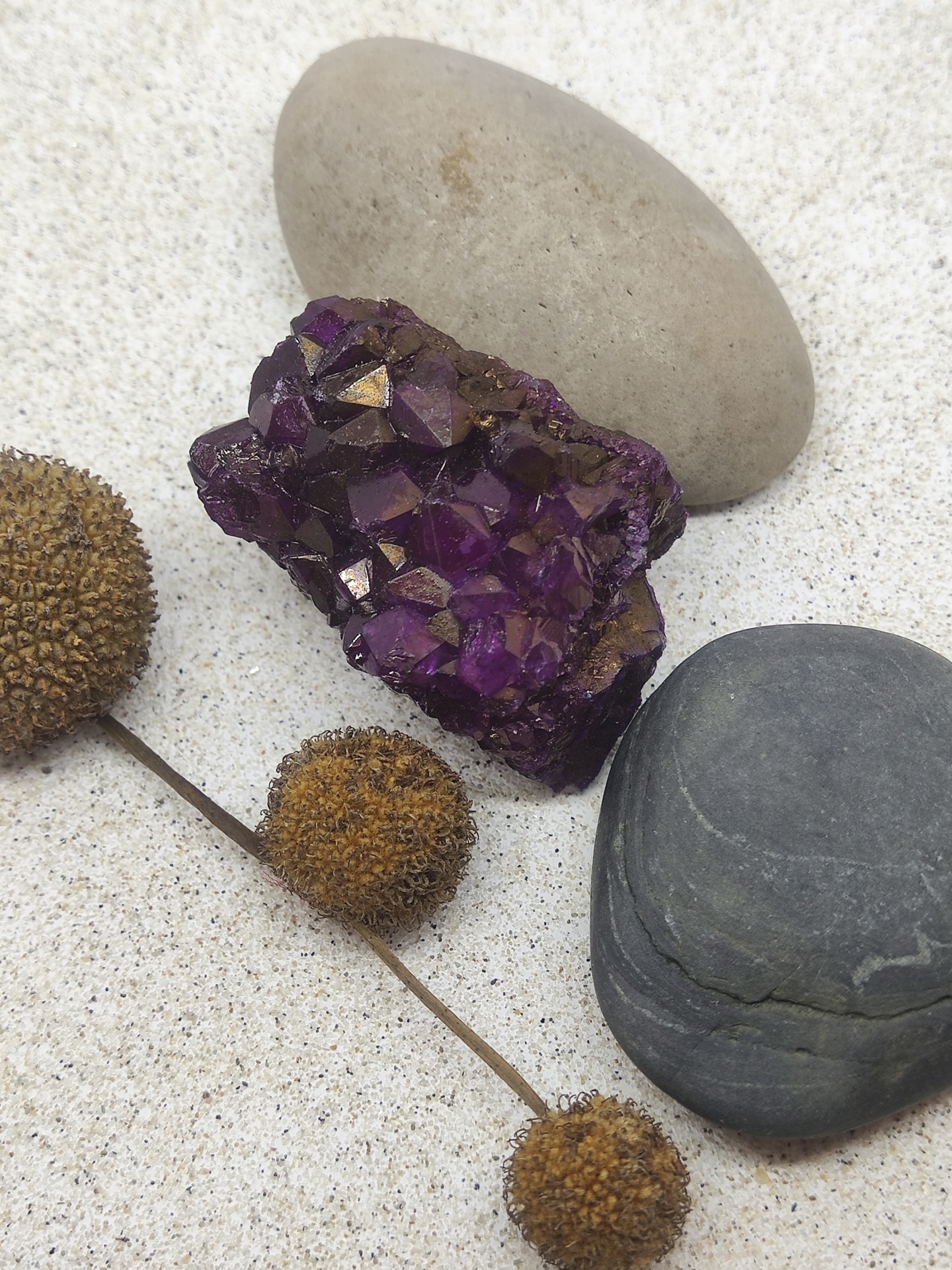 Cristal ametista roxo com pedras lisas e flores secas em areia clara