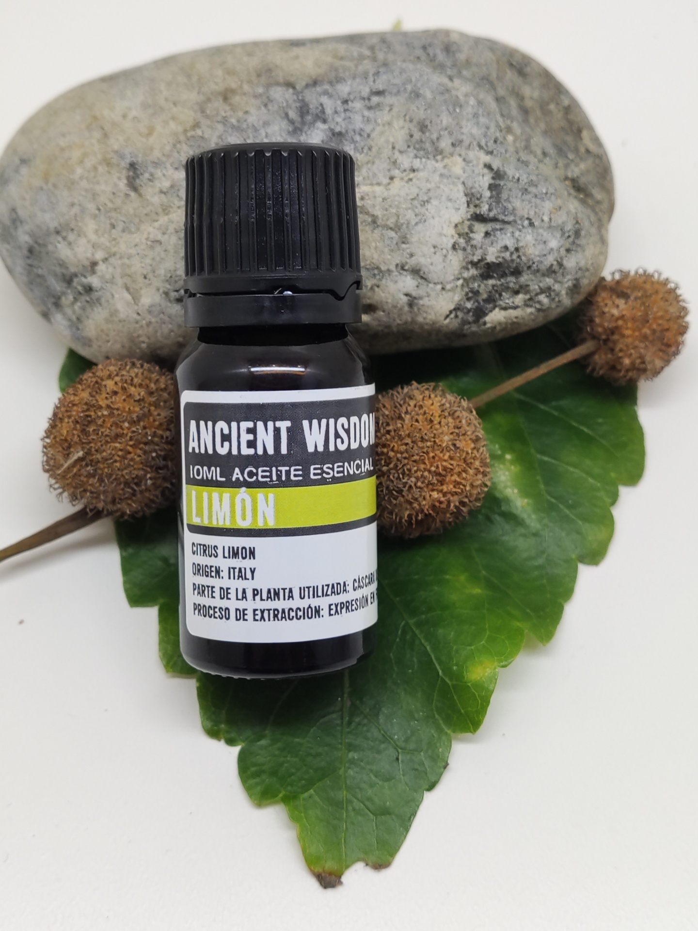 Frasco de óleo essencial de limão junto a uma pedra e folhas verdes