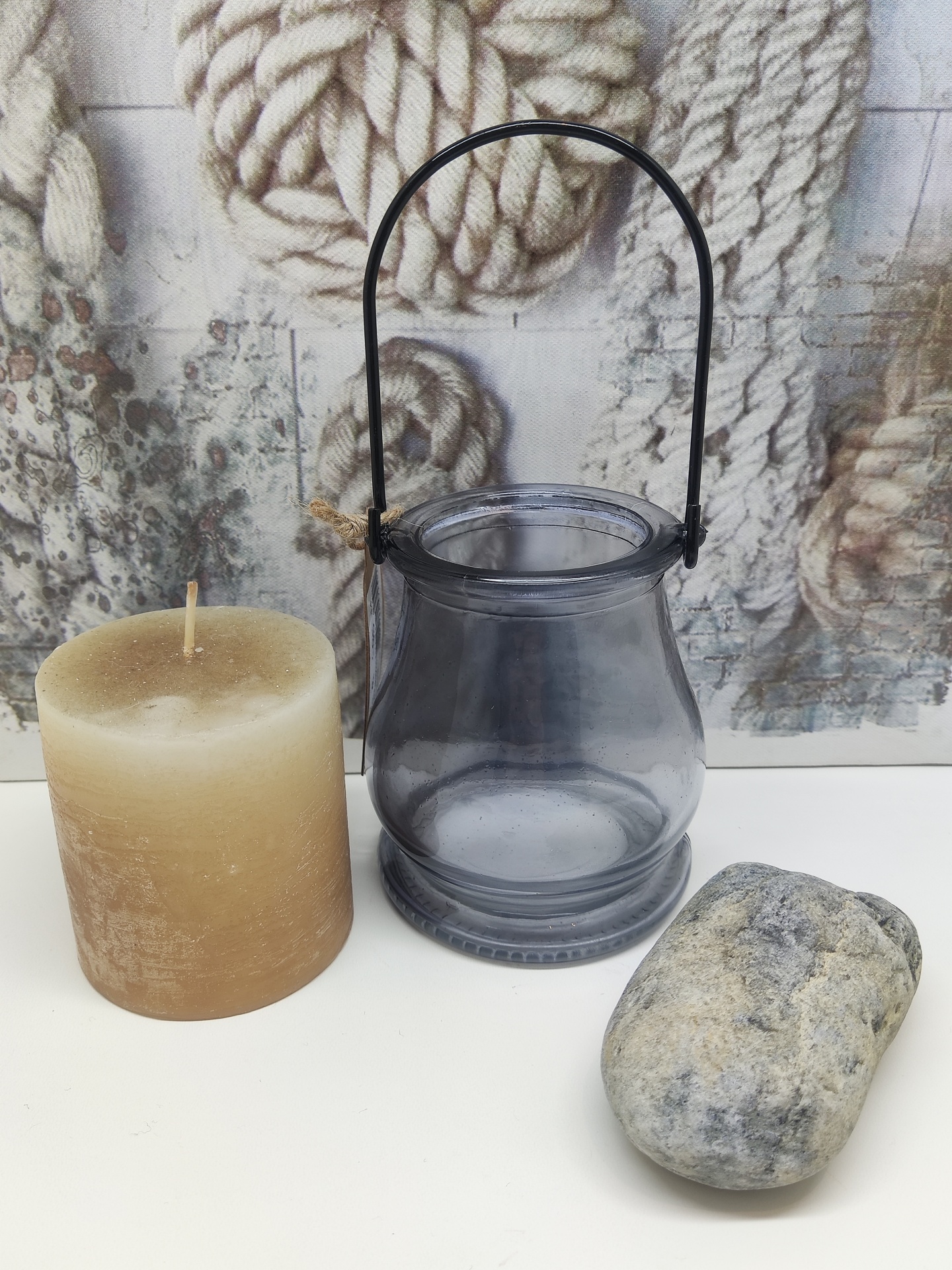 Vela castanha, suporte de vidro cinzento com alça preta e pedra cinzenta sobre superfície branca