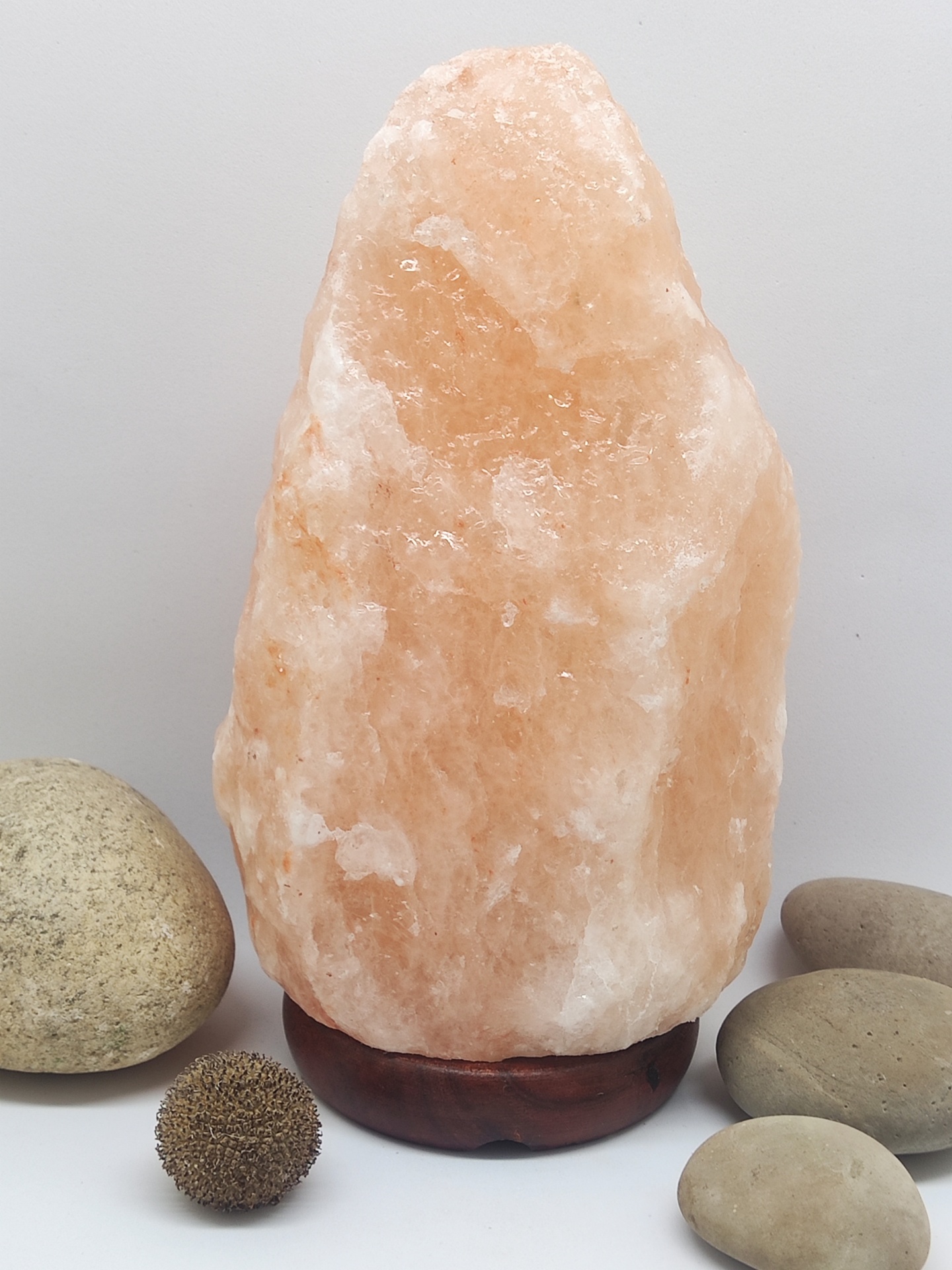 Lâmpada de sal rosa com base de madeira escura e pedras ao redor