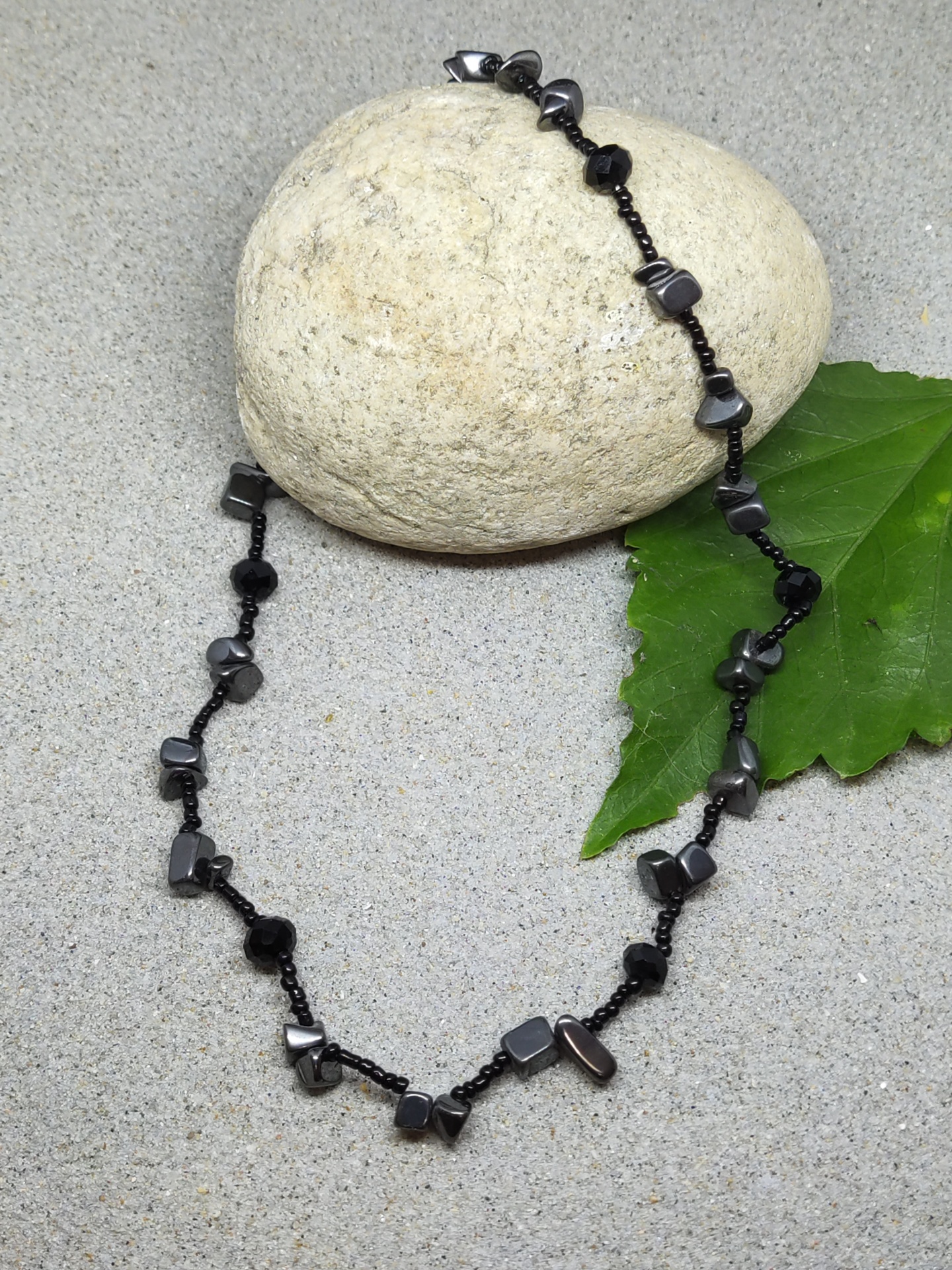 Colar com pedras pretas e cinzentas sobre pedra clara e folha verde