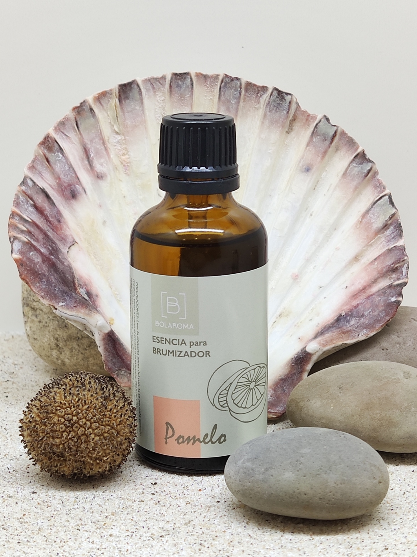 Frasco âmbar para esência de brumizador com etiqueta branca, ao lado de concha e pedras