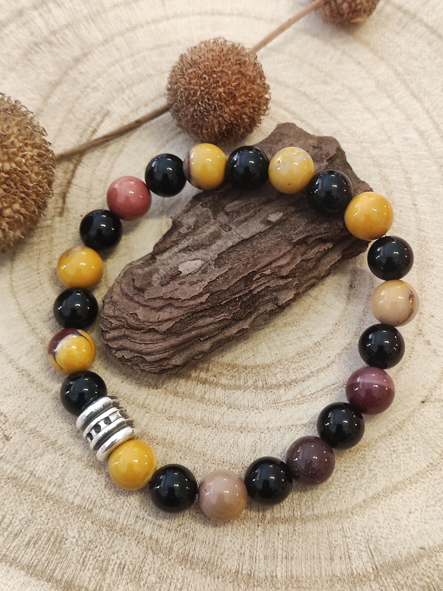 Pulseira de contas coloridas com peça metálica sobre madeira seca e elementos naturais