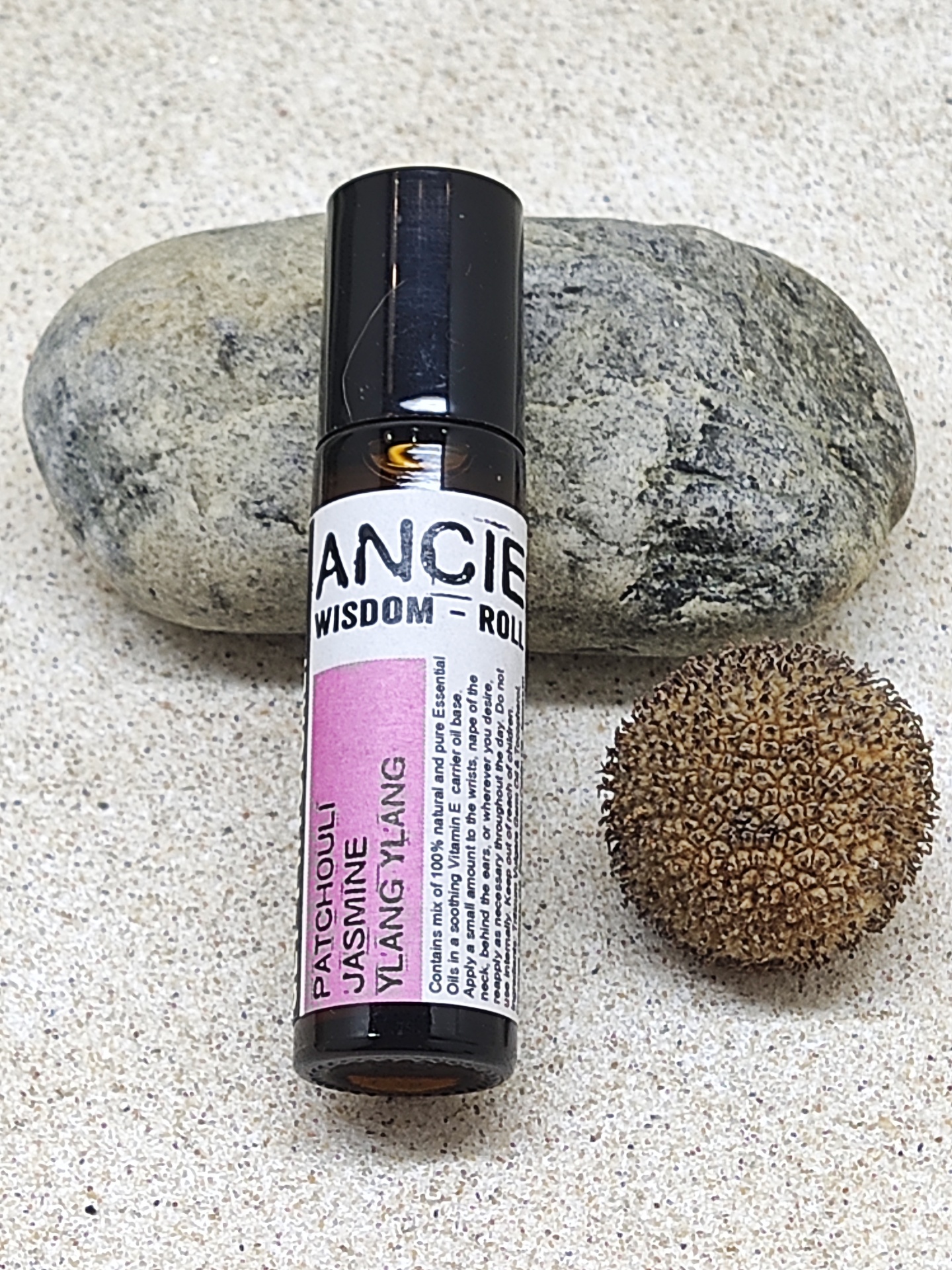 Frasco pequeno de vidro escuro com rótulo colorido ao lado de uma pedra e uma semente