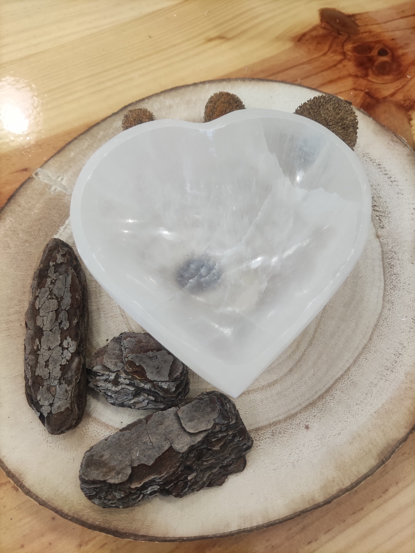 Prato de madeira claro com cascas de árvore e um recipiente translúcido branco em forma de coração no centro