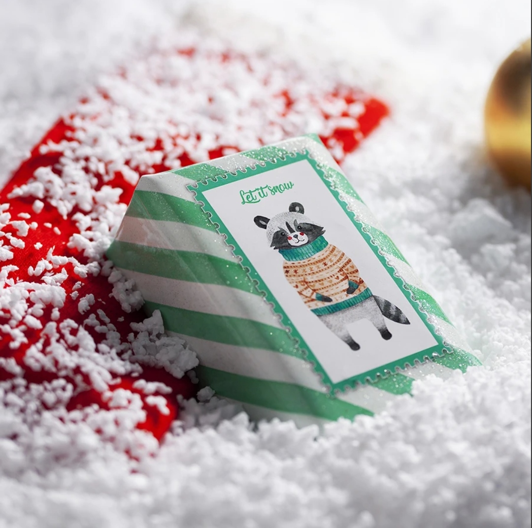 Pacote pequeno com papel verde às riscas brancas e autocolante de guaxinim com camisola