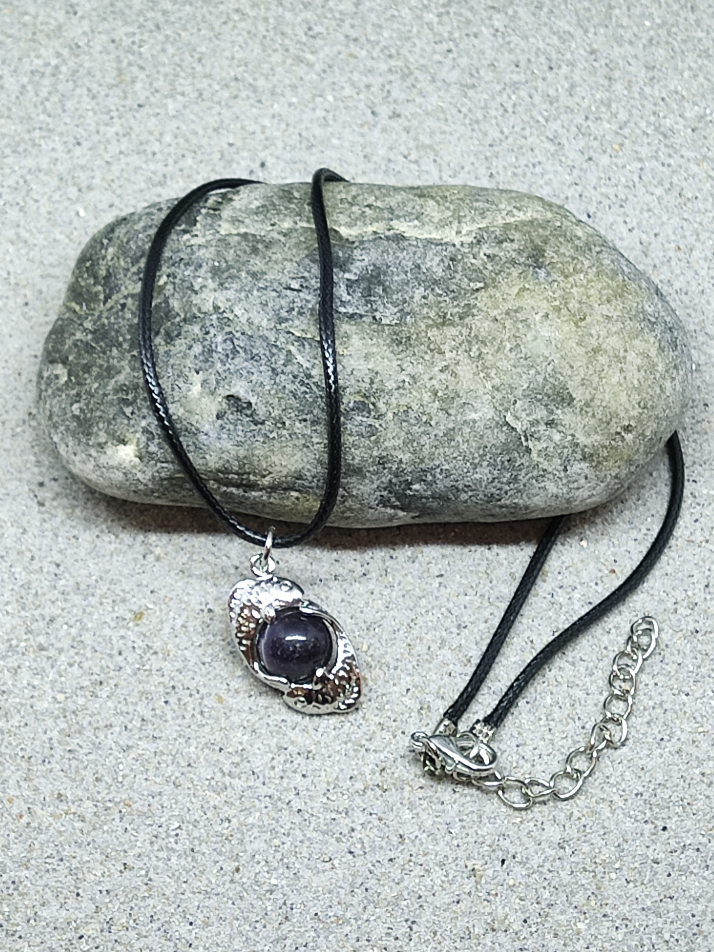 Colar com pendente metálico prateado e pedra escura sobre pedra cinzenta