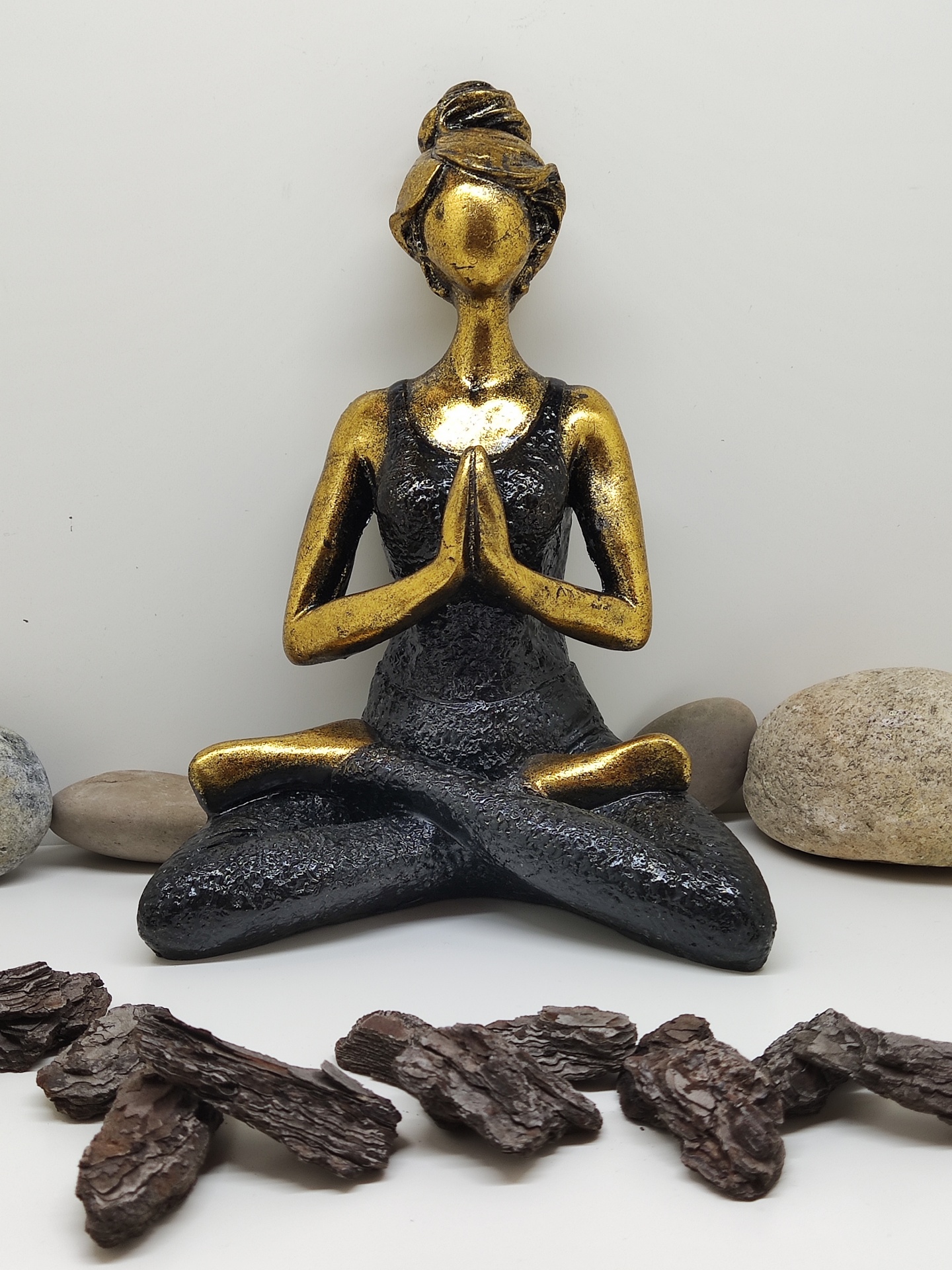 Estátua decorativa de mulher em meditação com pedras e madeira ao redor