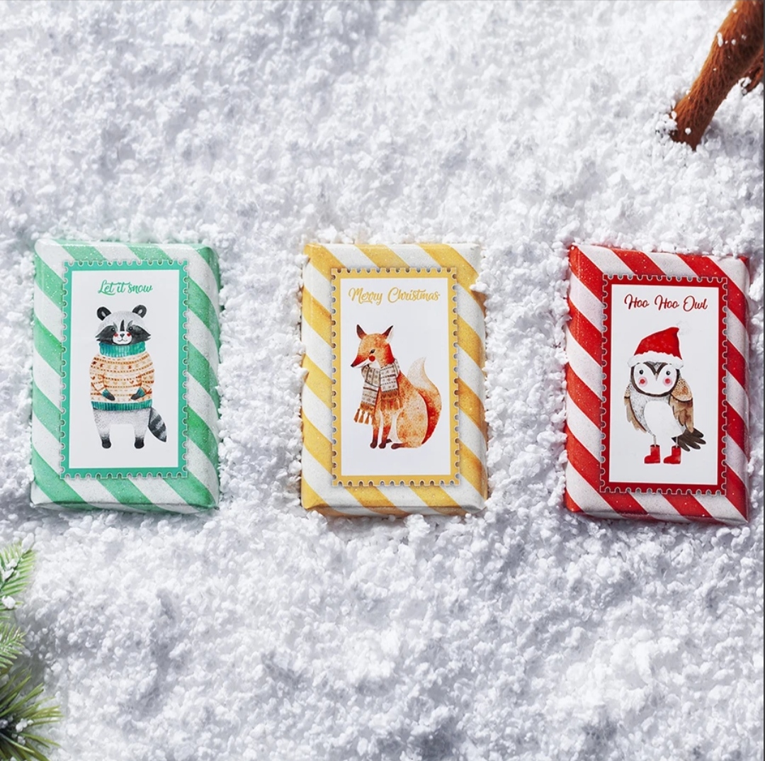 Três barras de chocolate com embalagens festivas e ilustrações de animais em neve.