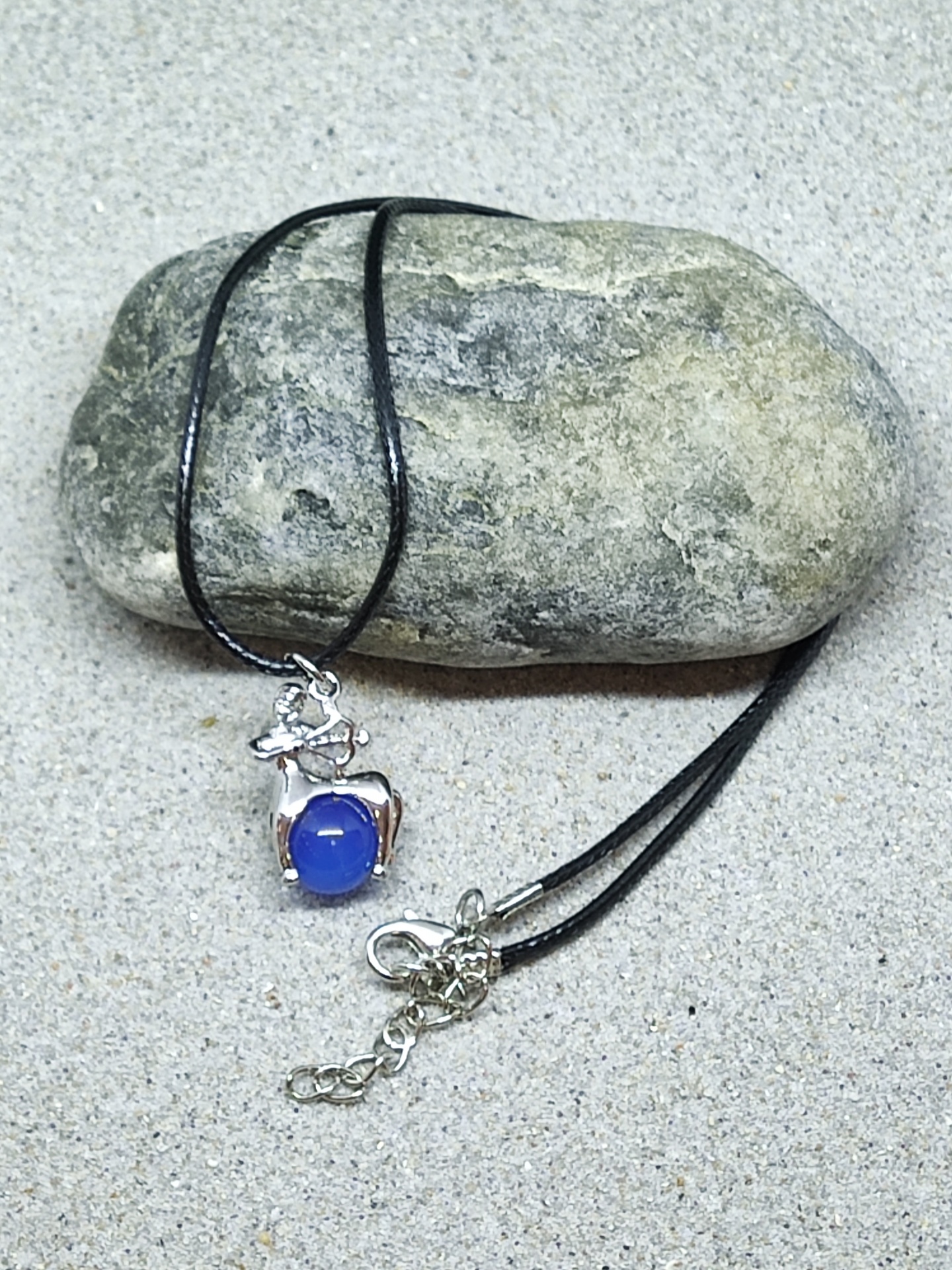 Colar com pendente de veado prateado e pedra azul numa pedra sobre areia