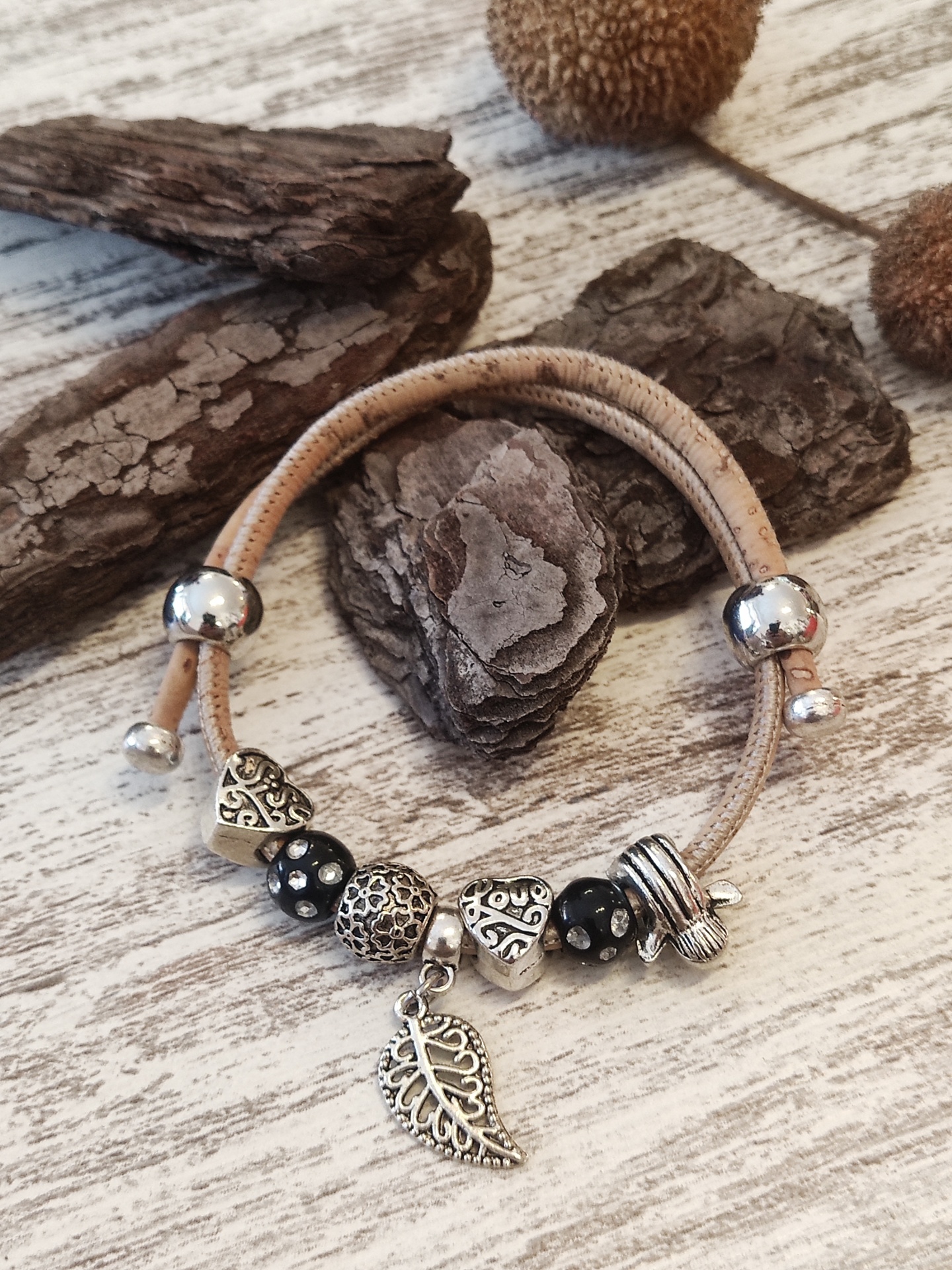 Pulseira com contas em metal prateado e cordão castanho claro sobre madeira