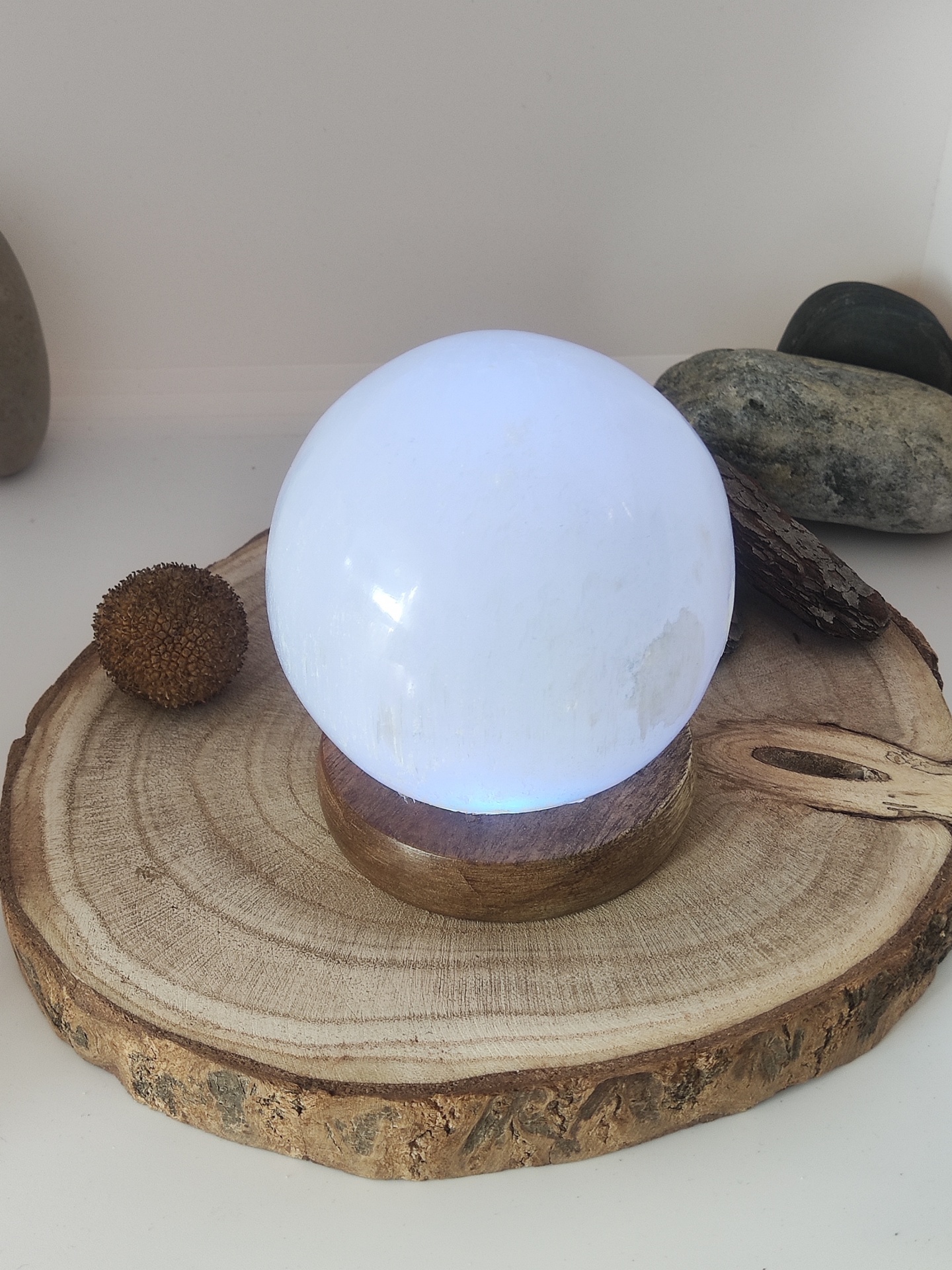Esfera de cristal branca em base de madeira sobre tronco com pedras ao fundo
