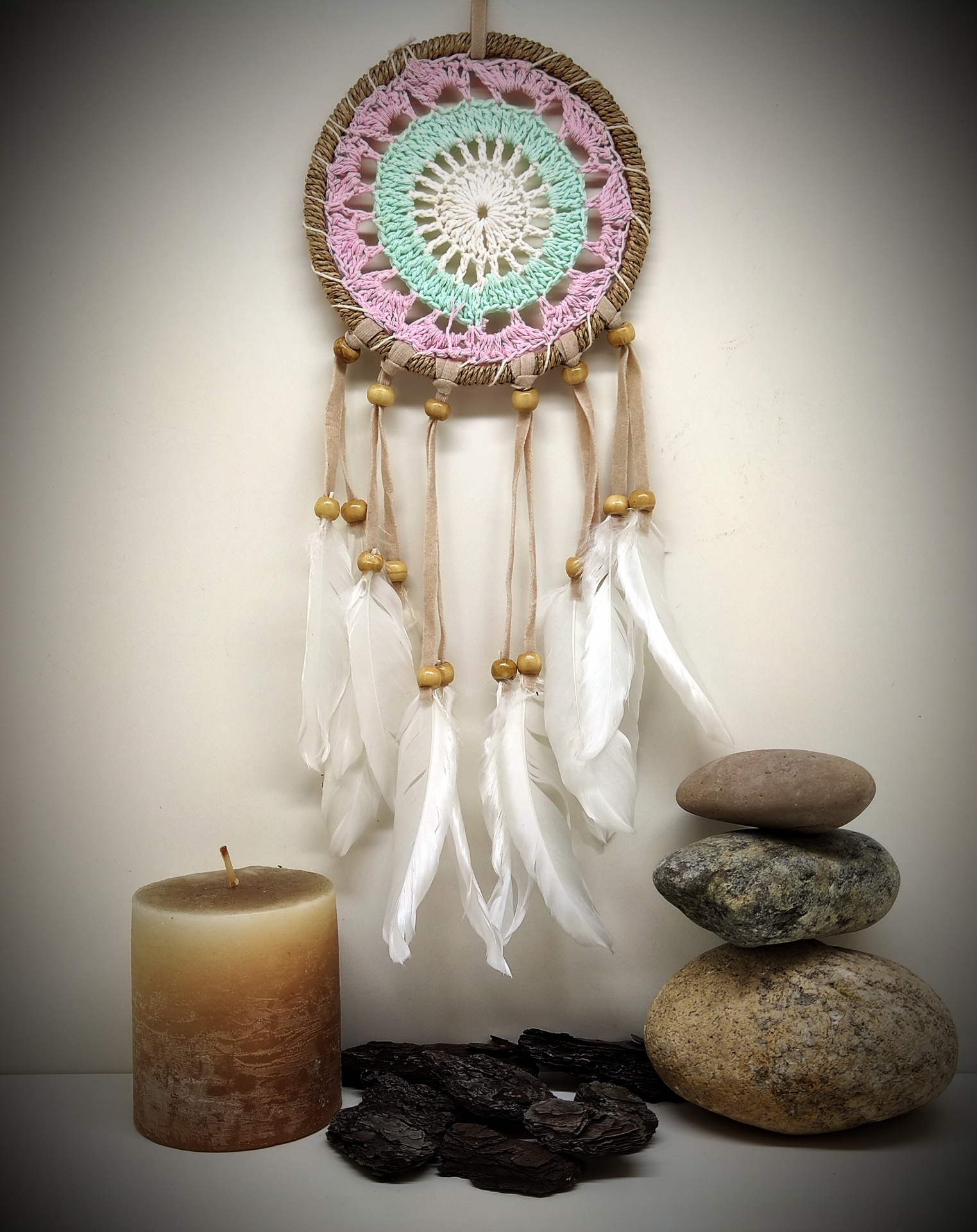 Filtro dos sonhos colorido com penas, vela, pedras empilhadas e pedaços de casca