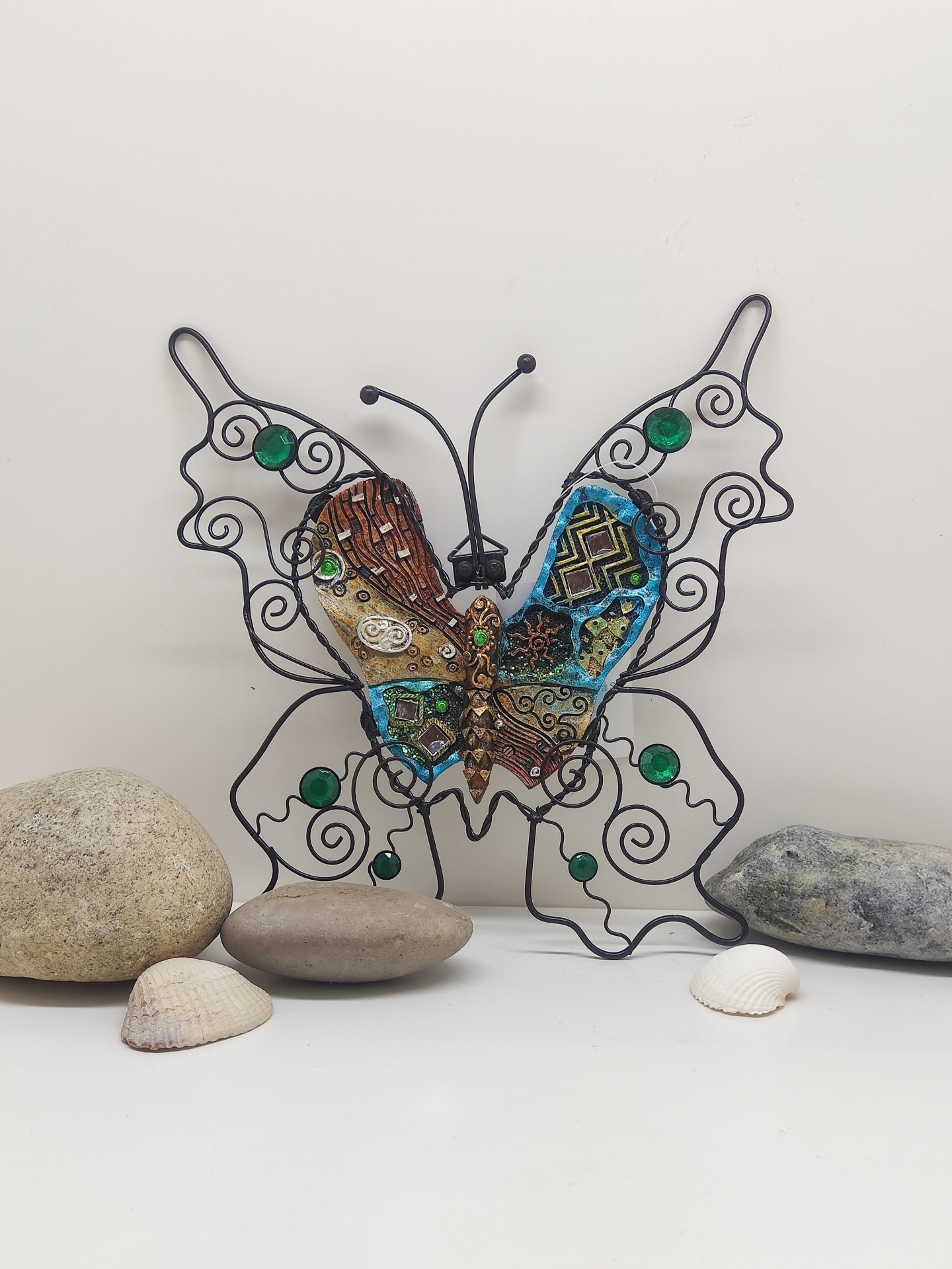 Escultura metálica de borboleta com pedras verdes e padrões multicoloridos