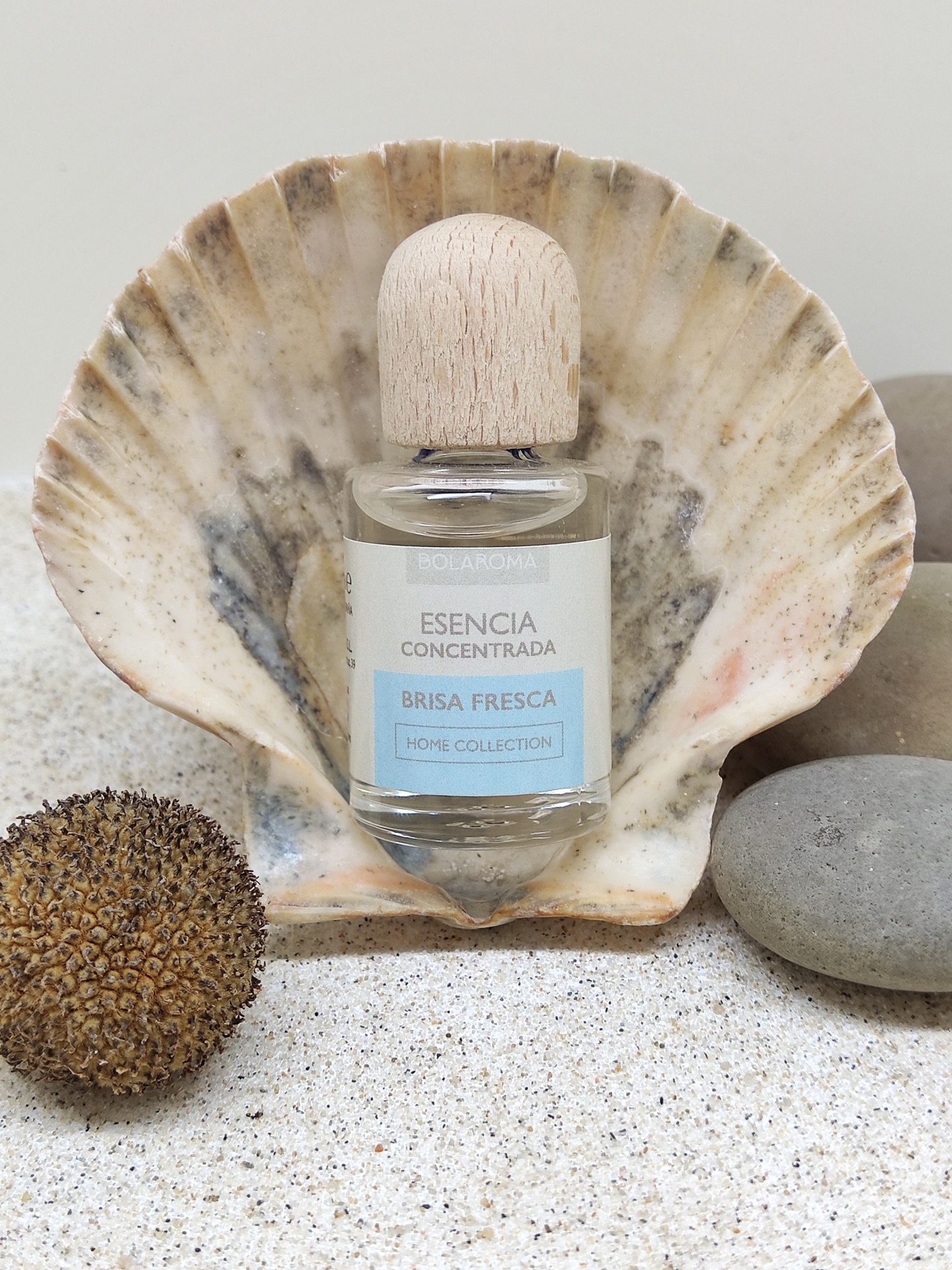 Frasco de essência concentrada Brisa Fresca sobre concha grande com pedras e areia