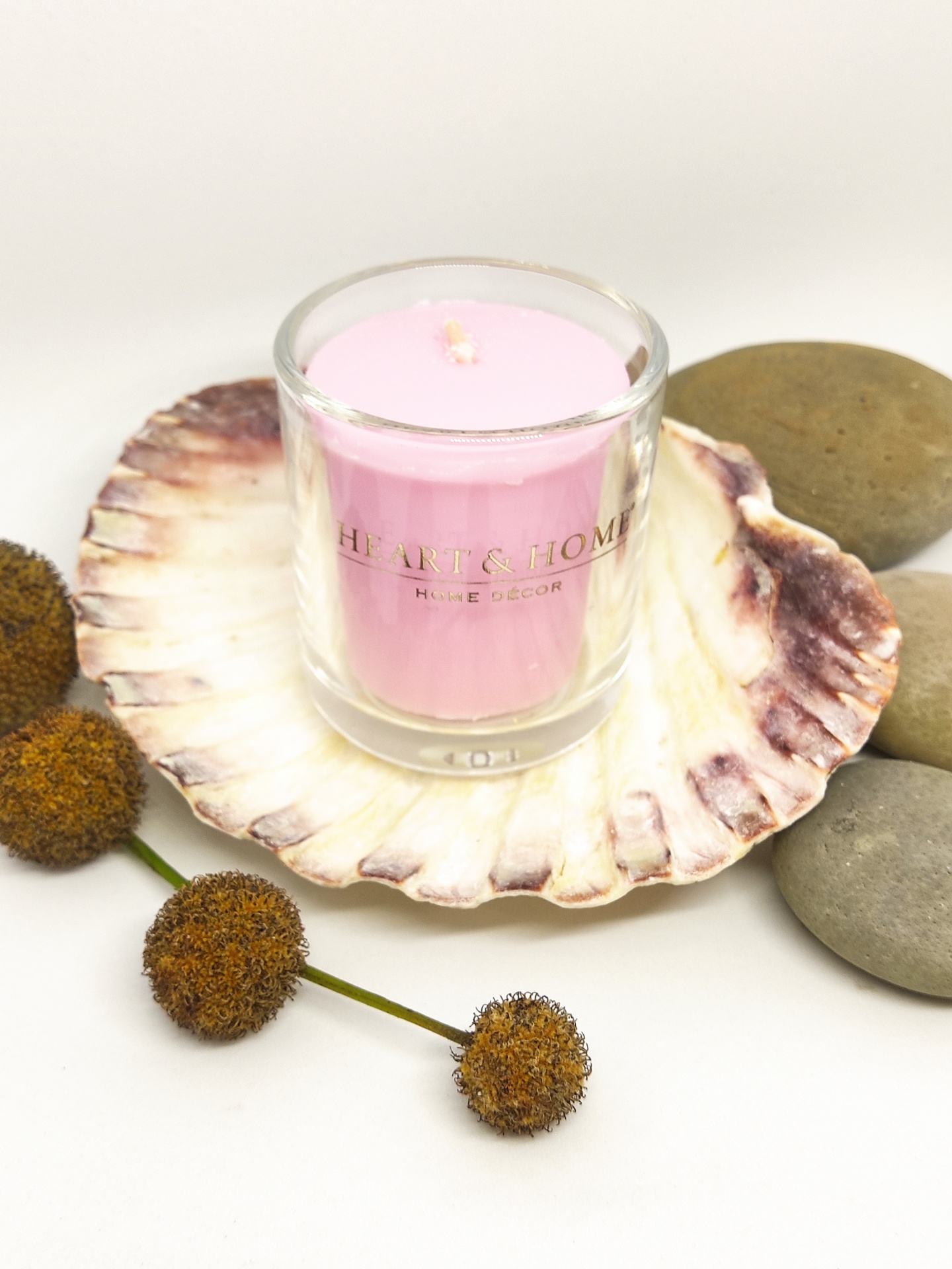 Vela rosa em copo de vidro dentro de concha com pedras e flores secas