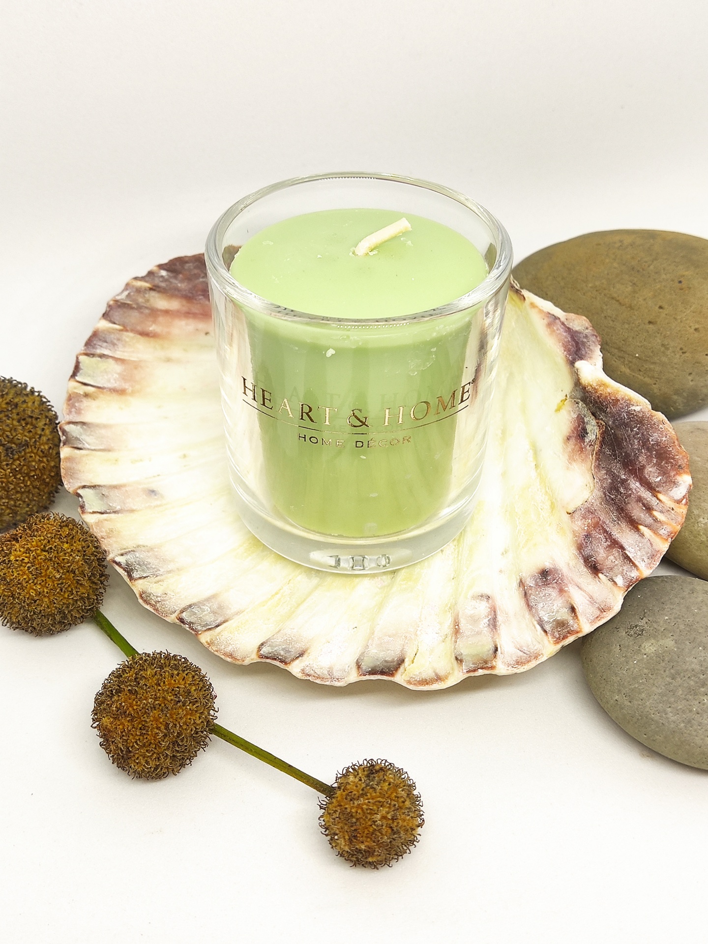 Vela verde em copo de vidro numa concha decorativa com pedras e flores secas