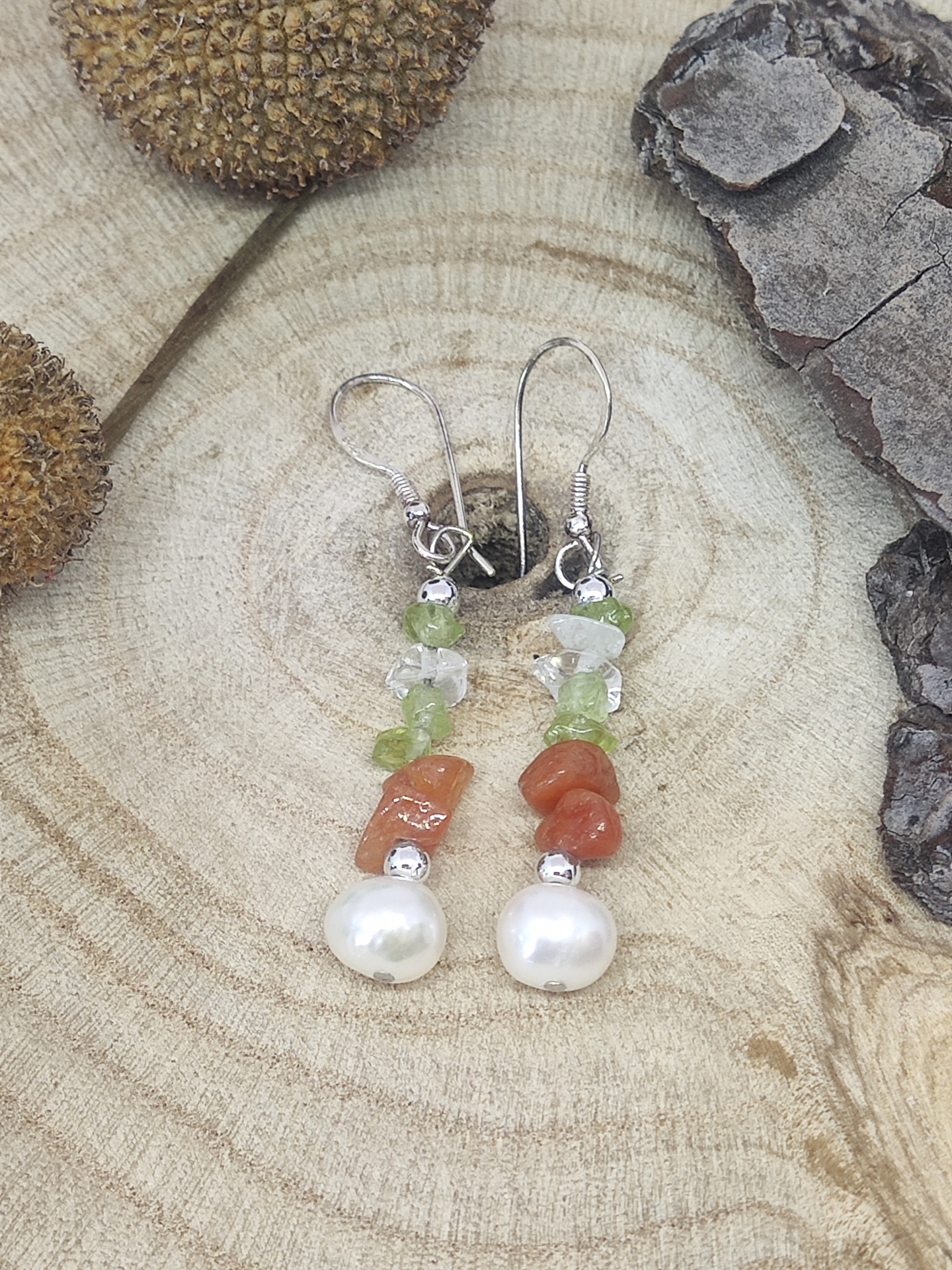 Brincos pendentes com pedras verdes e castanhas e pérola sobre madeira