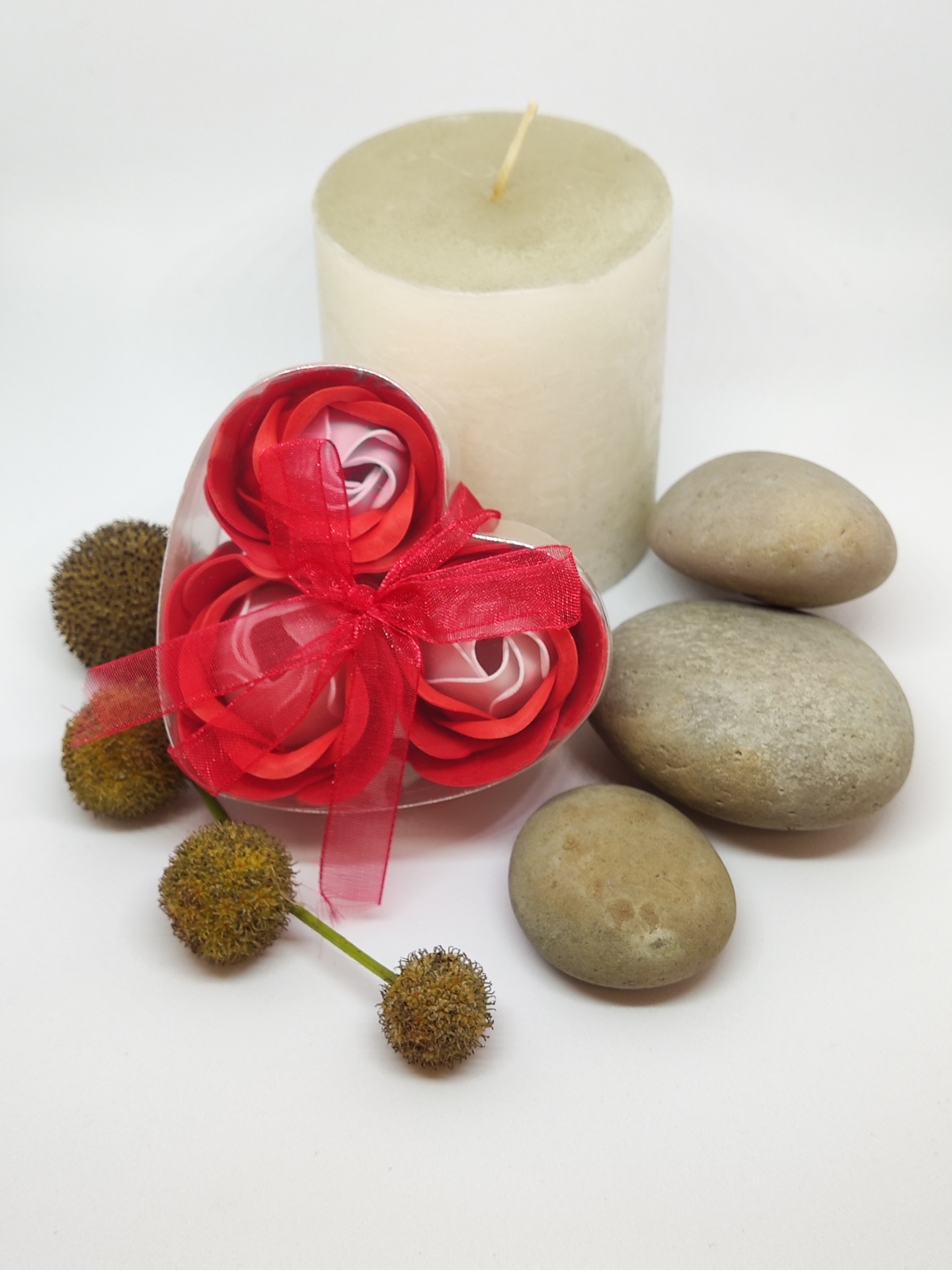 Vela branca com flores artificiais em embalagem de coração, pedras lisas e flores secas num fundo branco