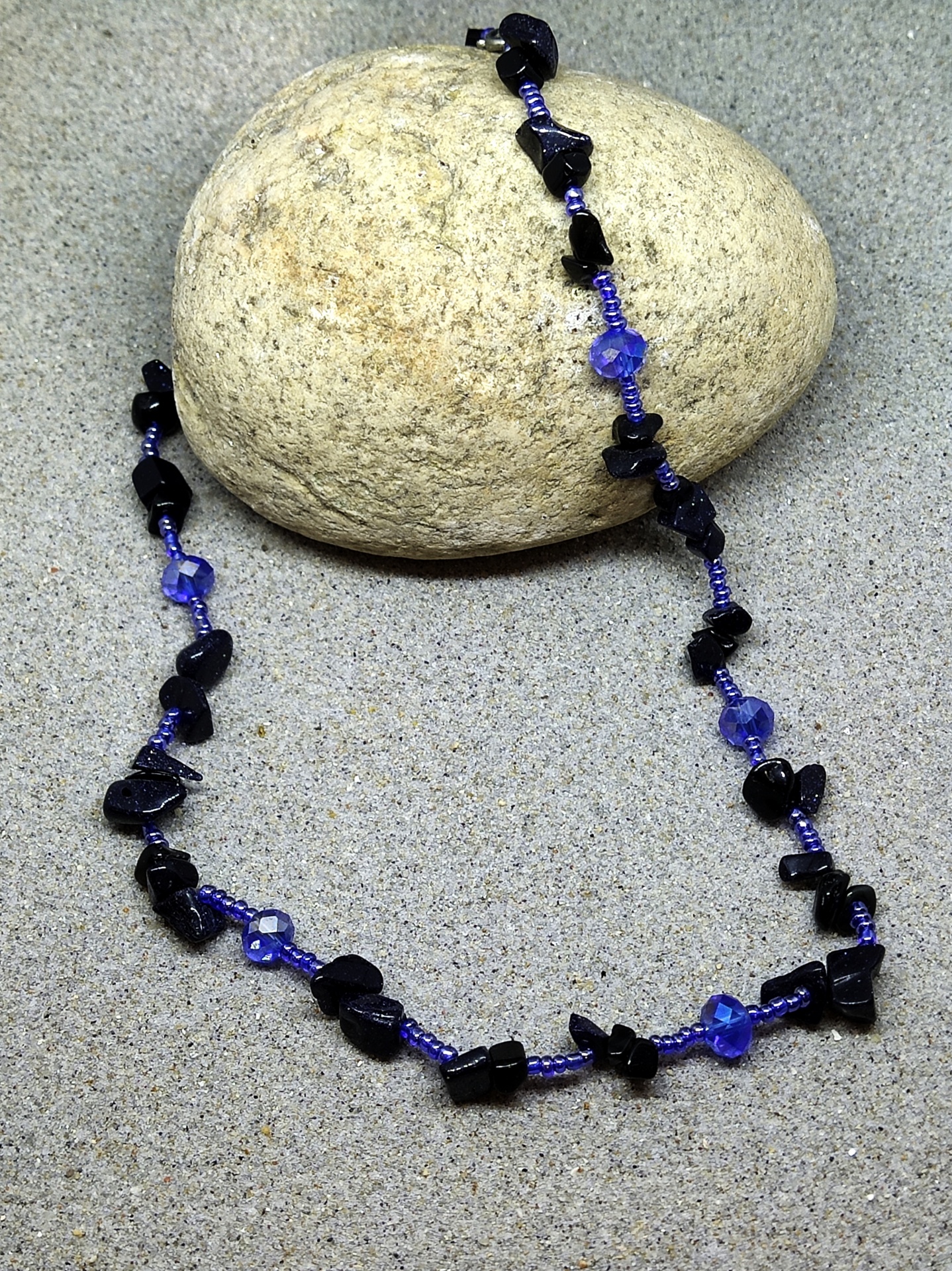 Colar azul com pedras pretas sobre areia e pedra clara