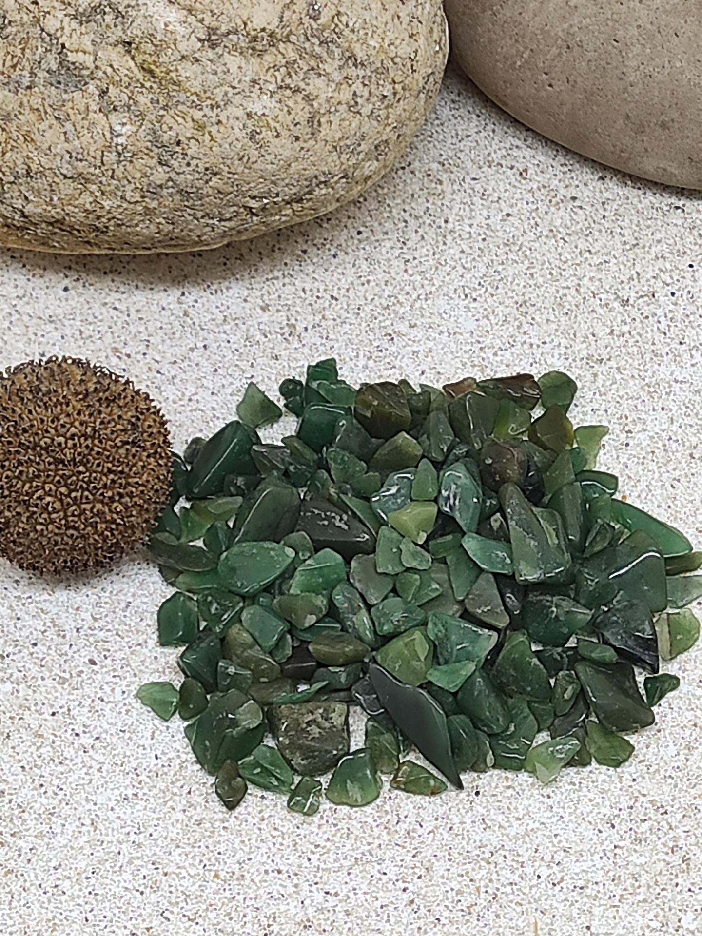 Pedras verdes irregulares com pedras grandes e esfera marrom numa superfície clara.