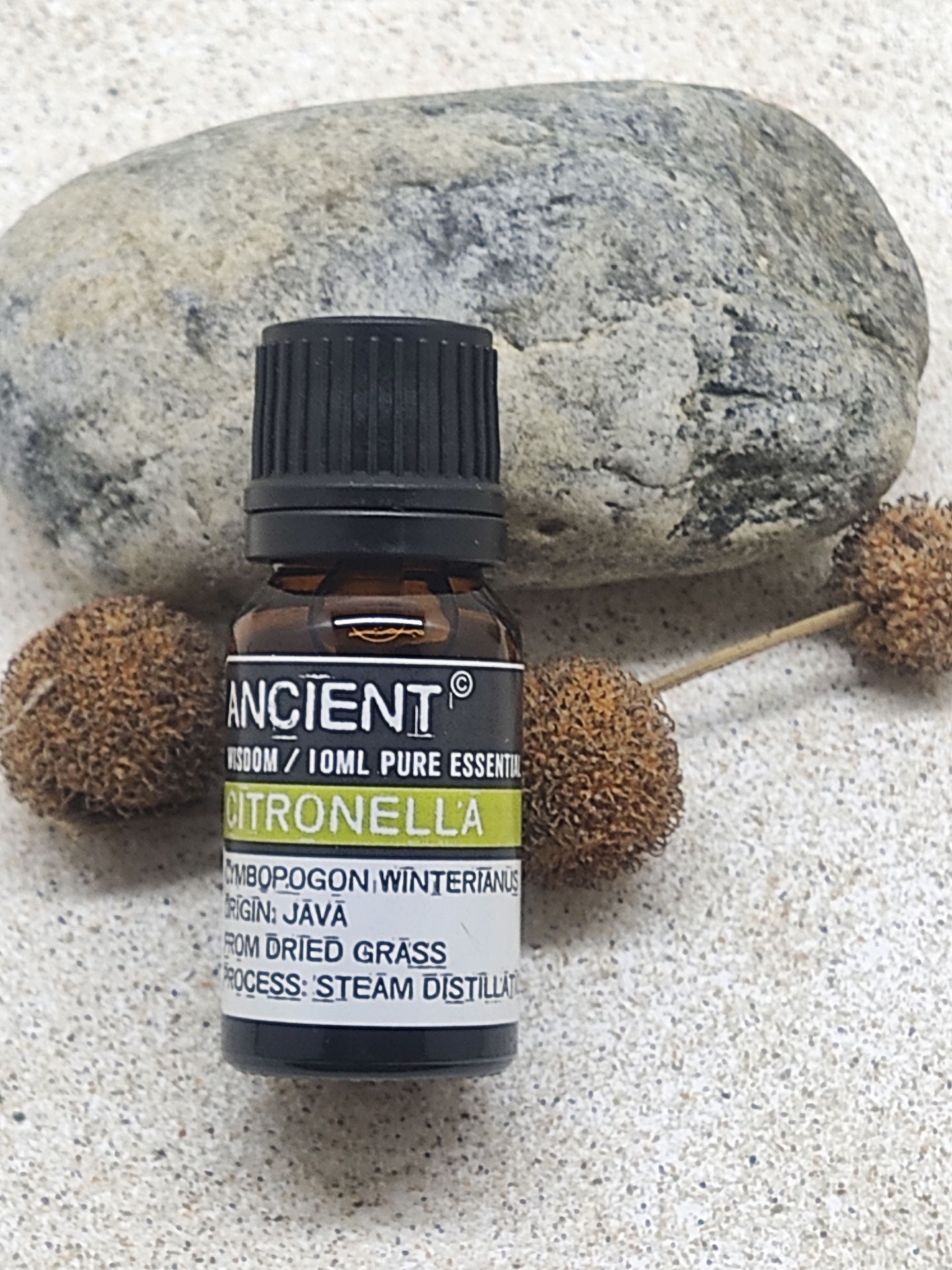 Frasco de óleo essencial de citronela ao lado de pedra e bolinhas secas