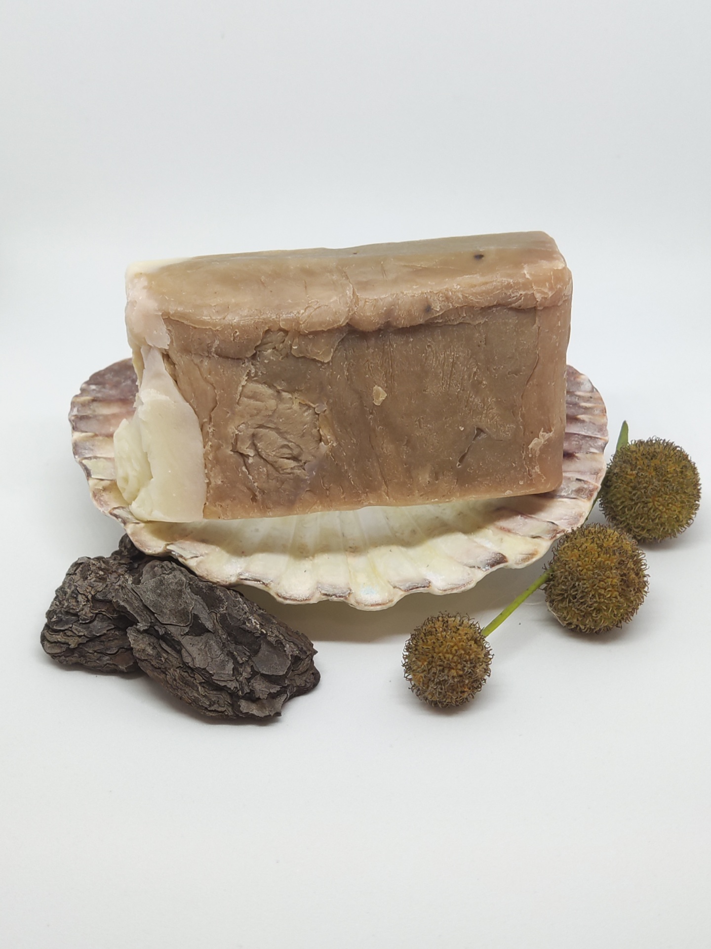 Barra de sabão castanha em concha branca com flores secas e casca