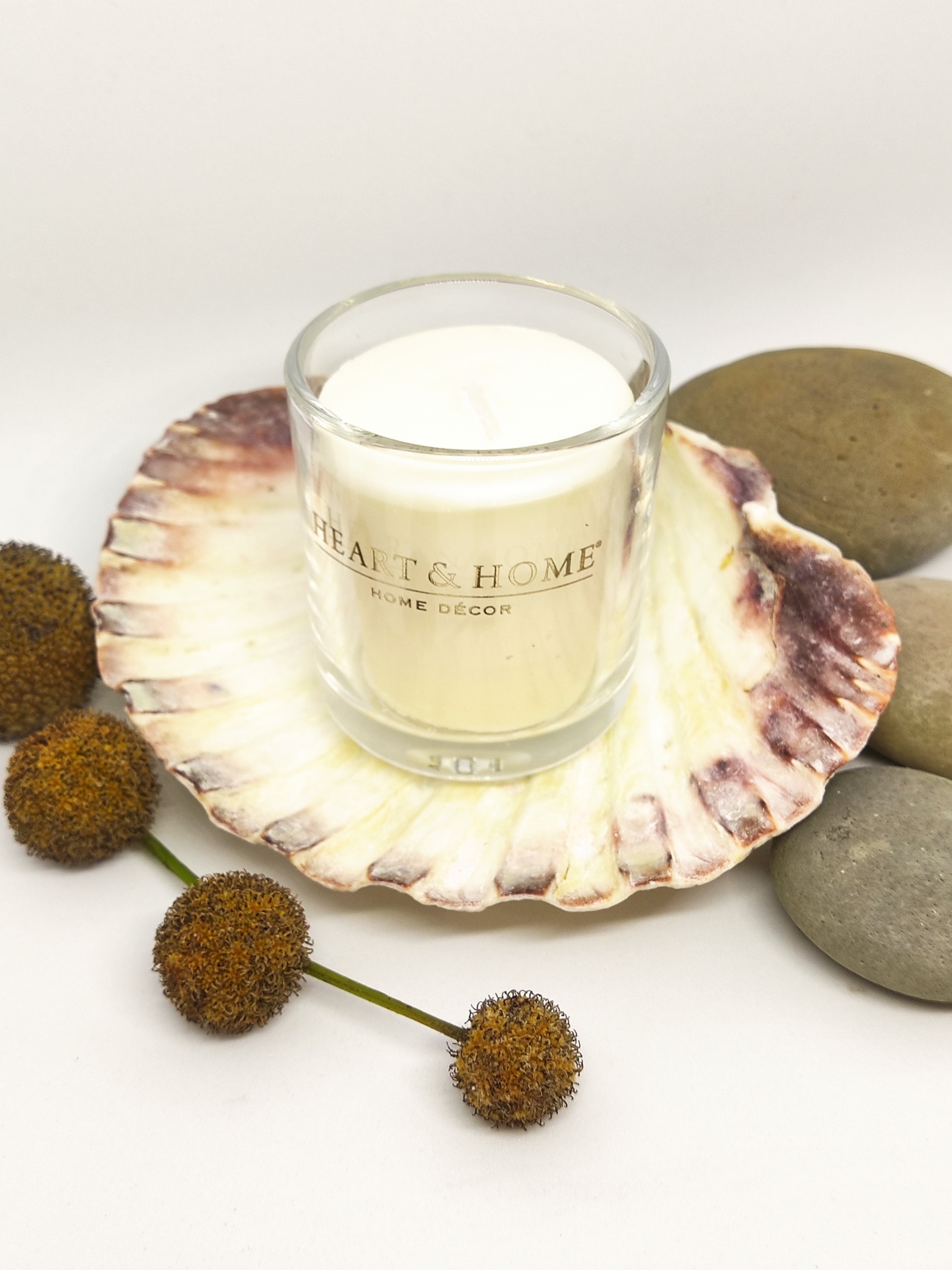 Vela em copo de vidro sobre concha, pedras e flores secas