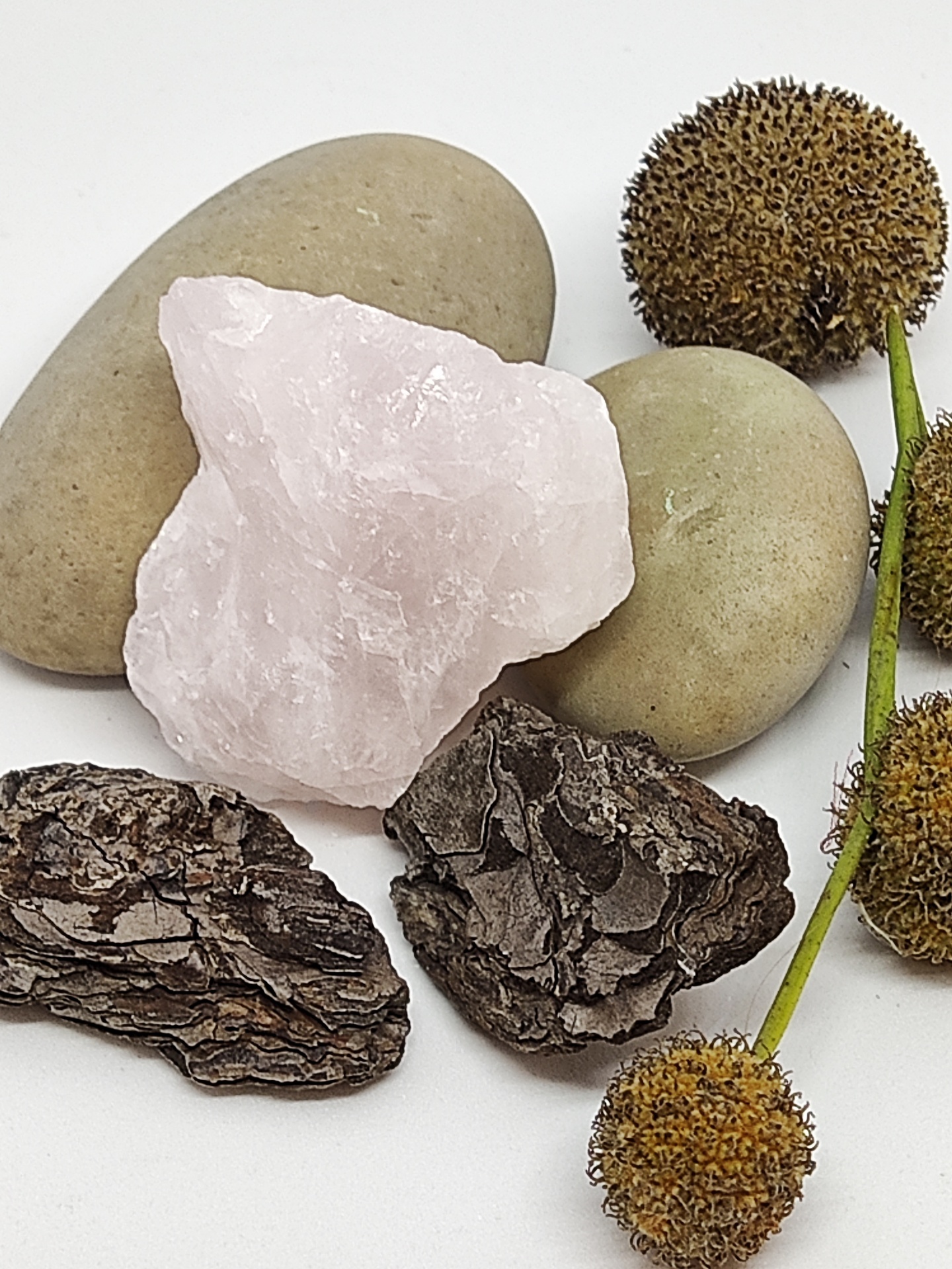 Pedras decorativas incluindo quartzo rosa, pedras lisas cinza, casca de árvore castanha e ramos com bolotas secas