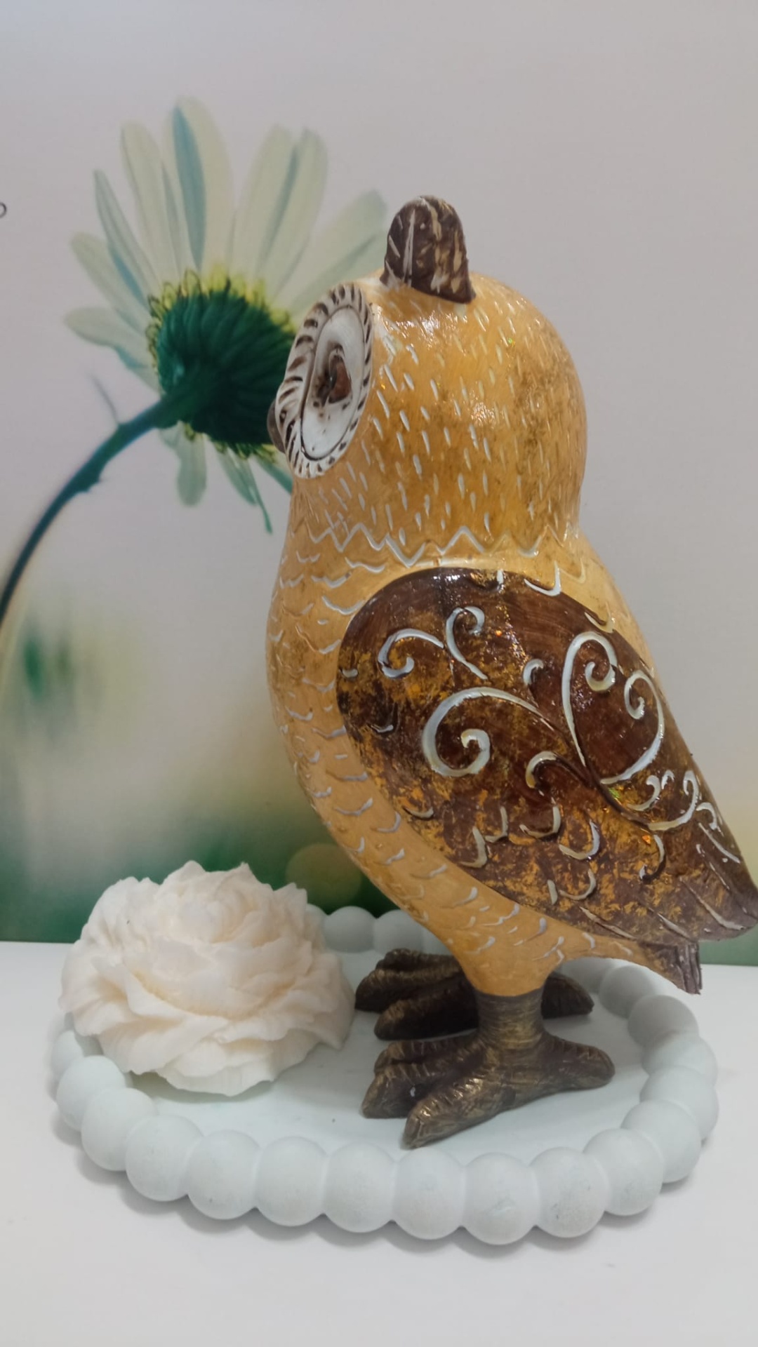 Escultura de coruja amarela e castanha numa base branca com flor decorativa