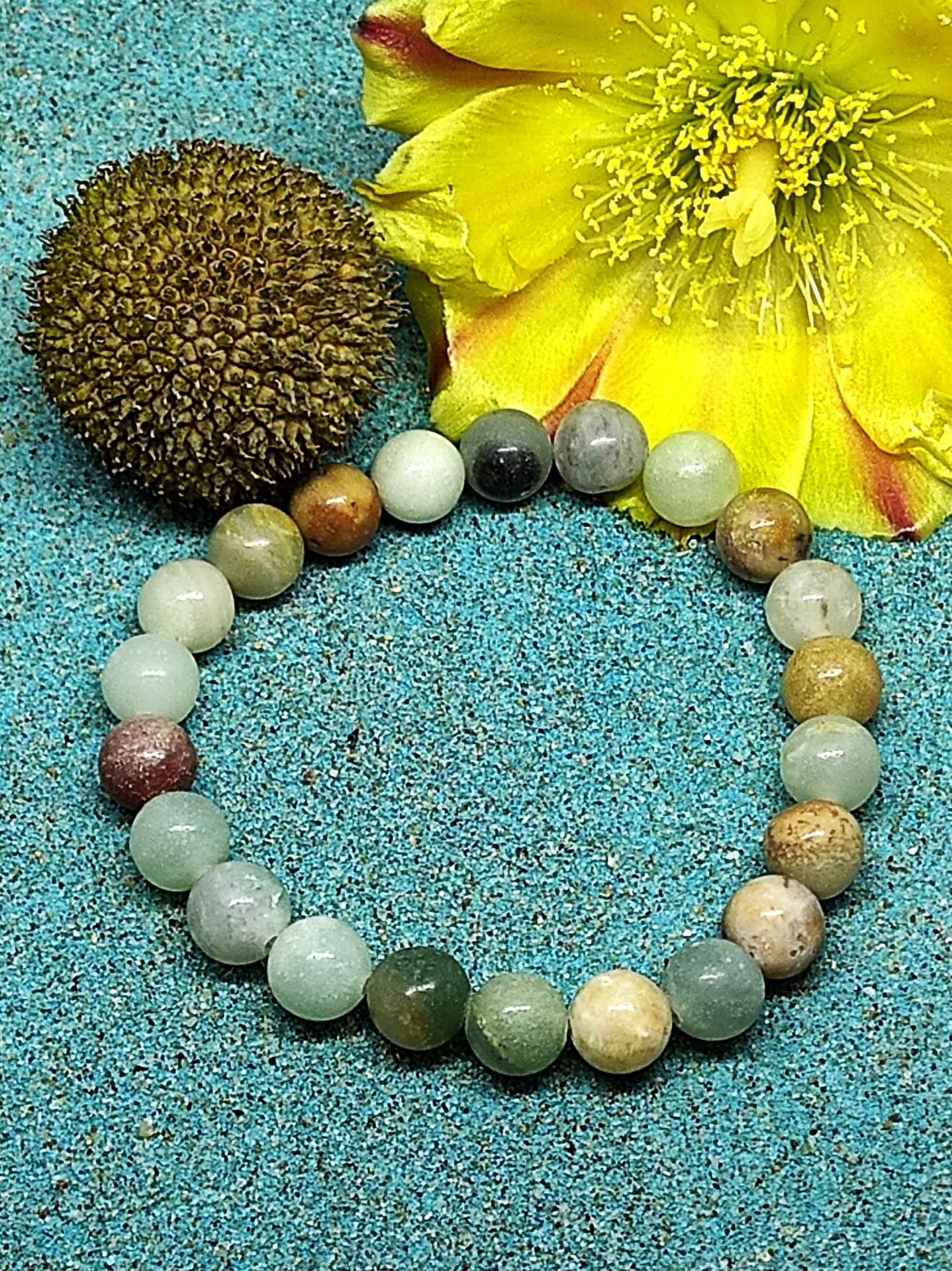 Pulseira de bolas coloridas de pedra natural com flor amarela e semente castanha em fundo azul