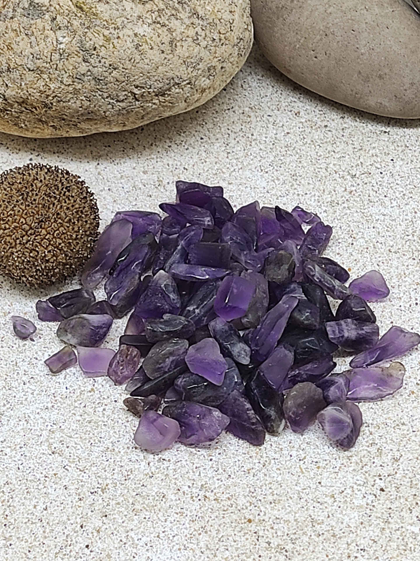 Pequenas pedras roxas sobre superfície clara, próximas a pedras arredondadas maiores e uma esfera castanha.