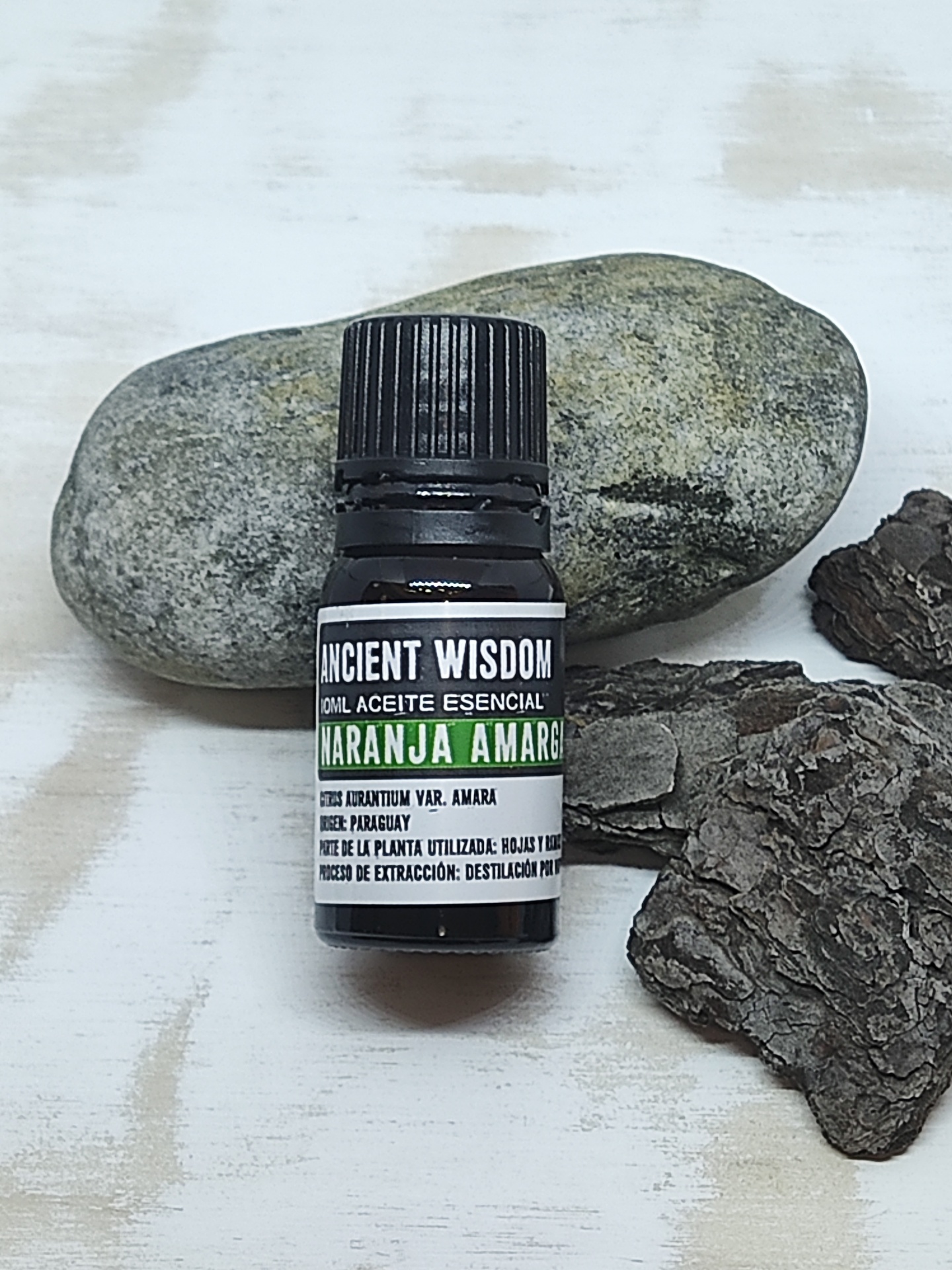 Frasco pequeno de óleo essencial com pedra e casca em superfície de madeira clara