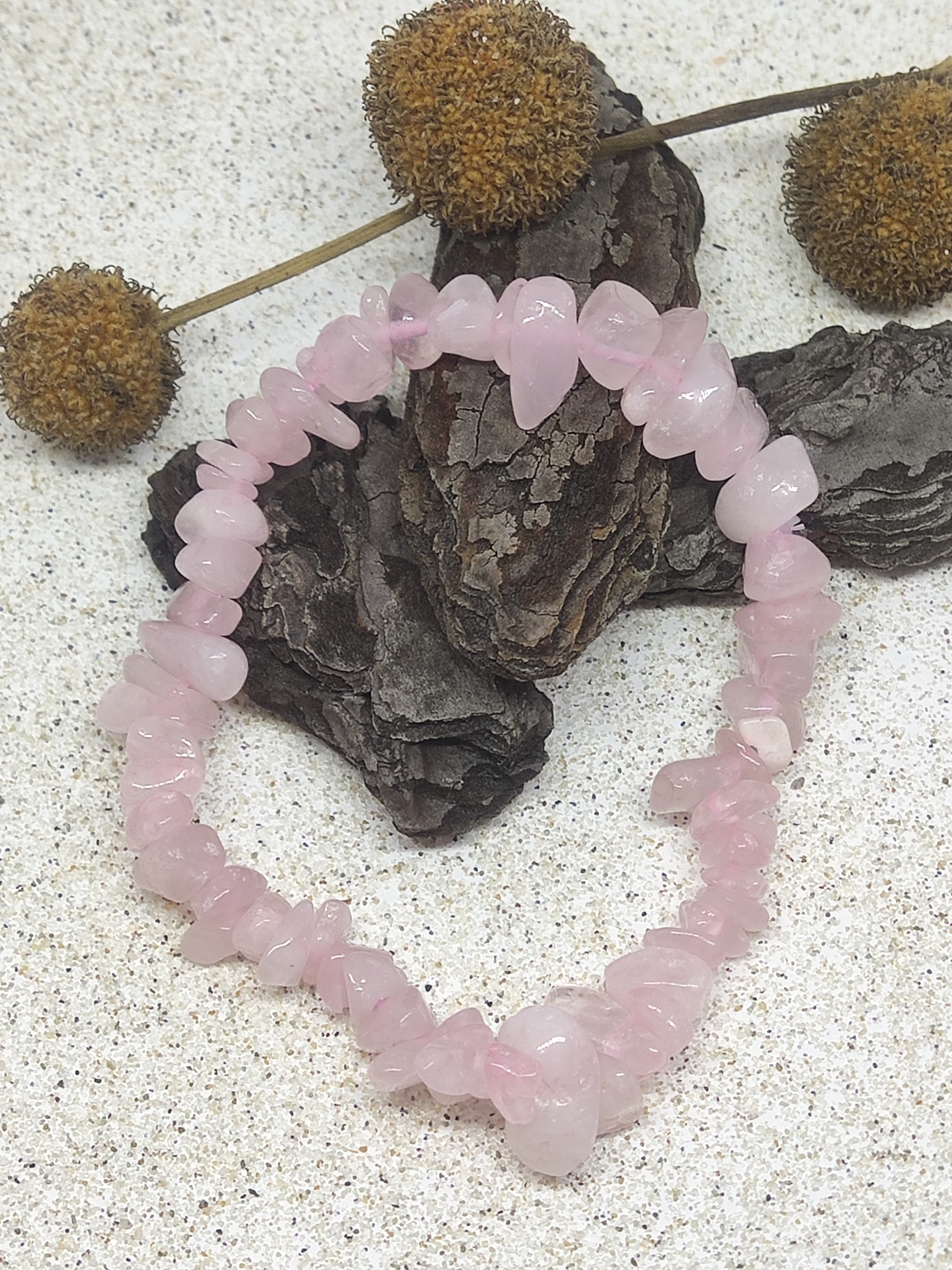 Pulseira de quartz rosa com pedras irregulares sobre fundo claro com casca e frutos secos
