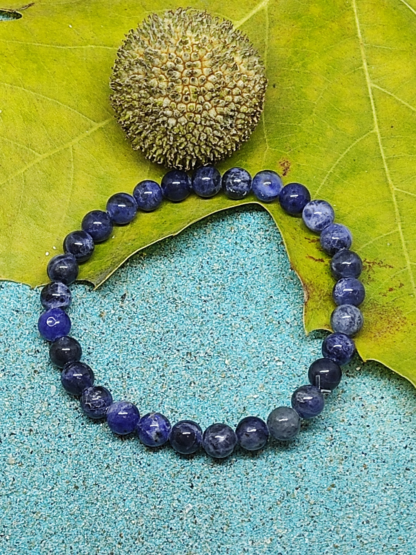Pulseira de contas de pedra azul com uma semente e folha verde sobre superfície azul