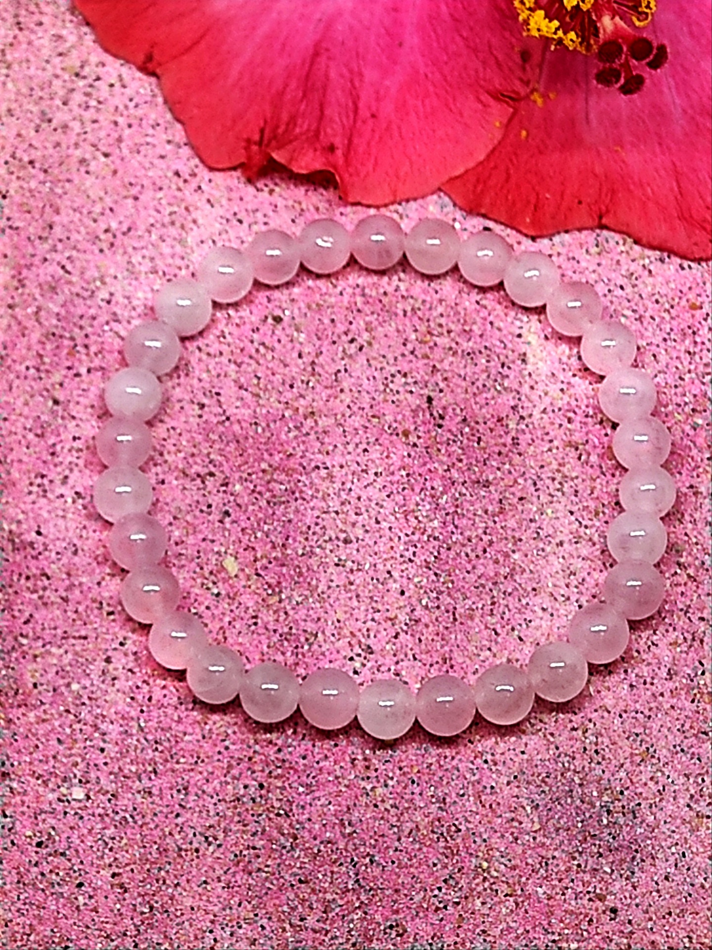 Pulseira de contas de quartzo rosa sobre fundo rosa com flor vermelha