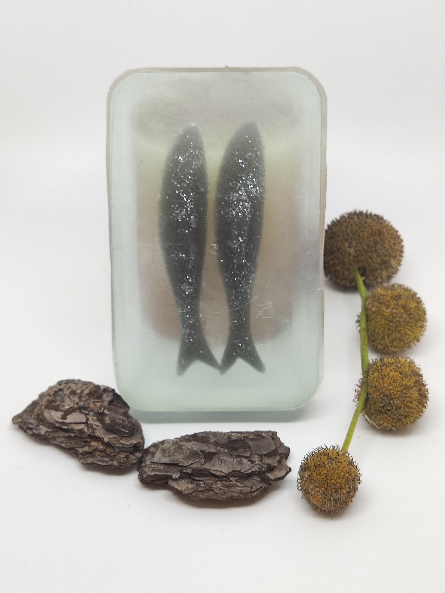 Sabonete transparente com duas figuras de peixes, cascas de árvore e ramo com frutos castanhos