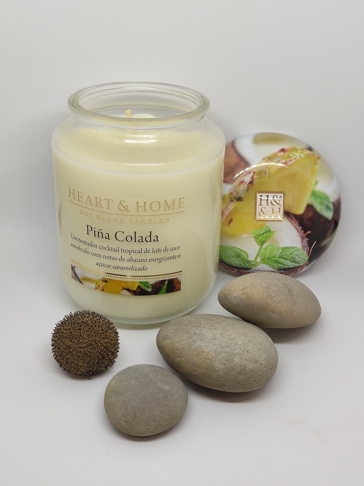 Vela perfumada HEART & HOME Piña Colada em vidro com tampa decorativa e pedras ao lado